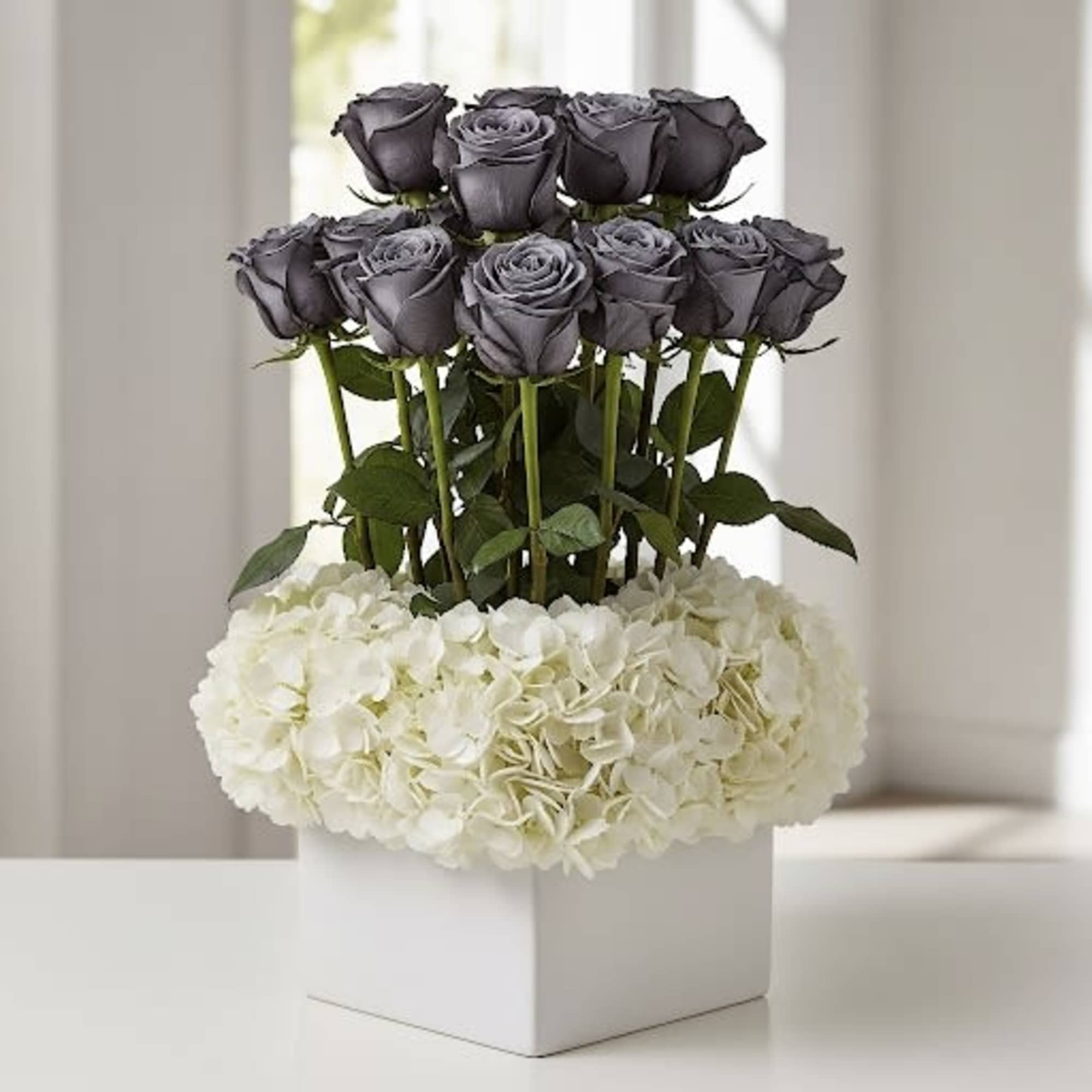 Dark roses above a white hydrangea arrangement in a square box