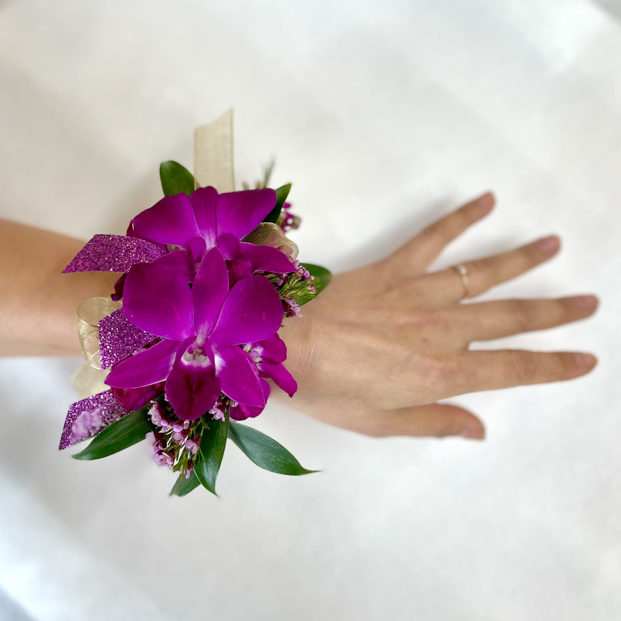 Fuchsia orchid wrist corsage with glitter ribbon worn on a hand