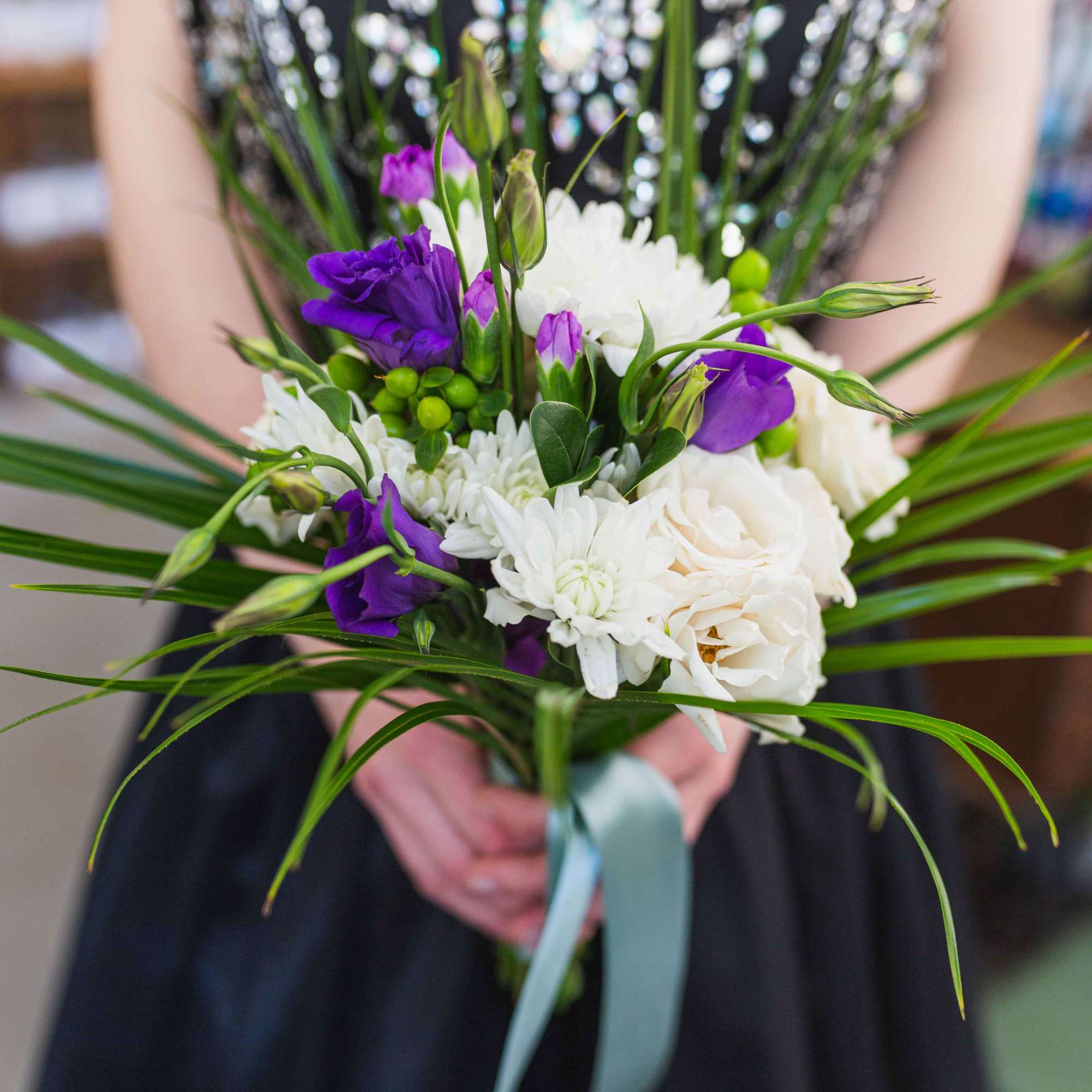Handheld bouquet of white and purple flowers with long grass-like leaves