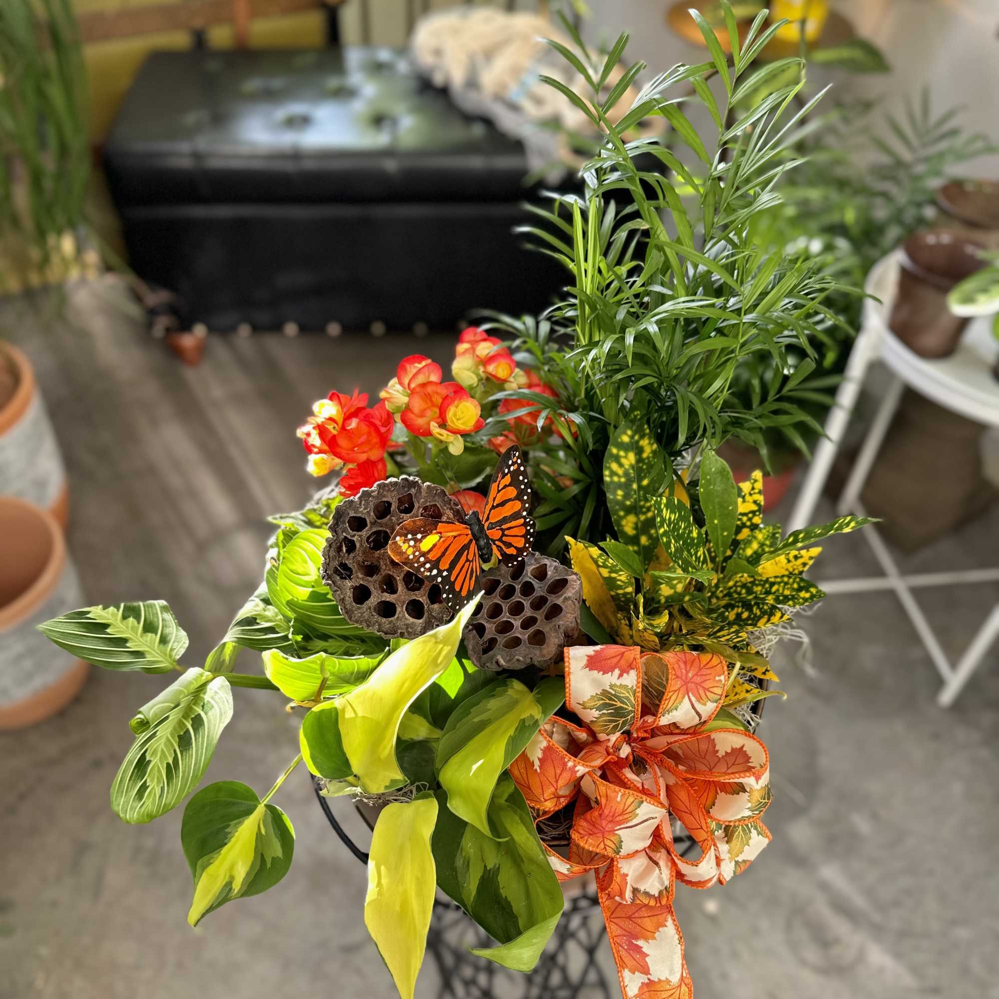 Tropical plant arrangement with orange flowers, a butterfly, and a fall ribbon