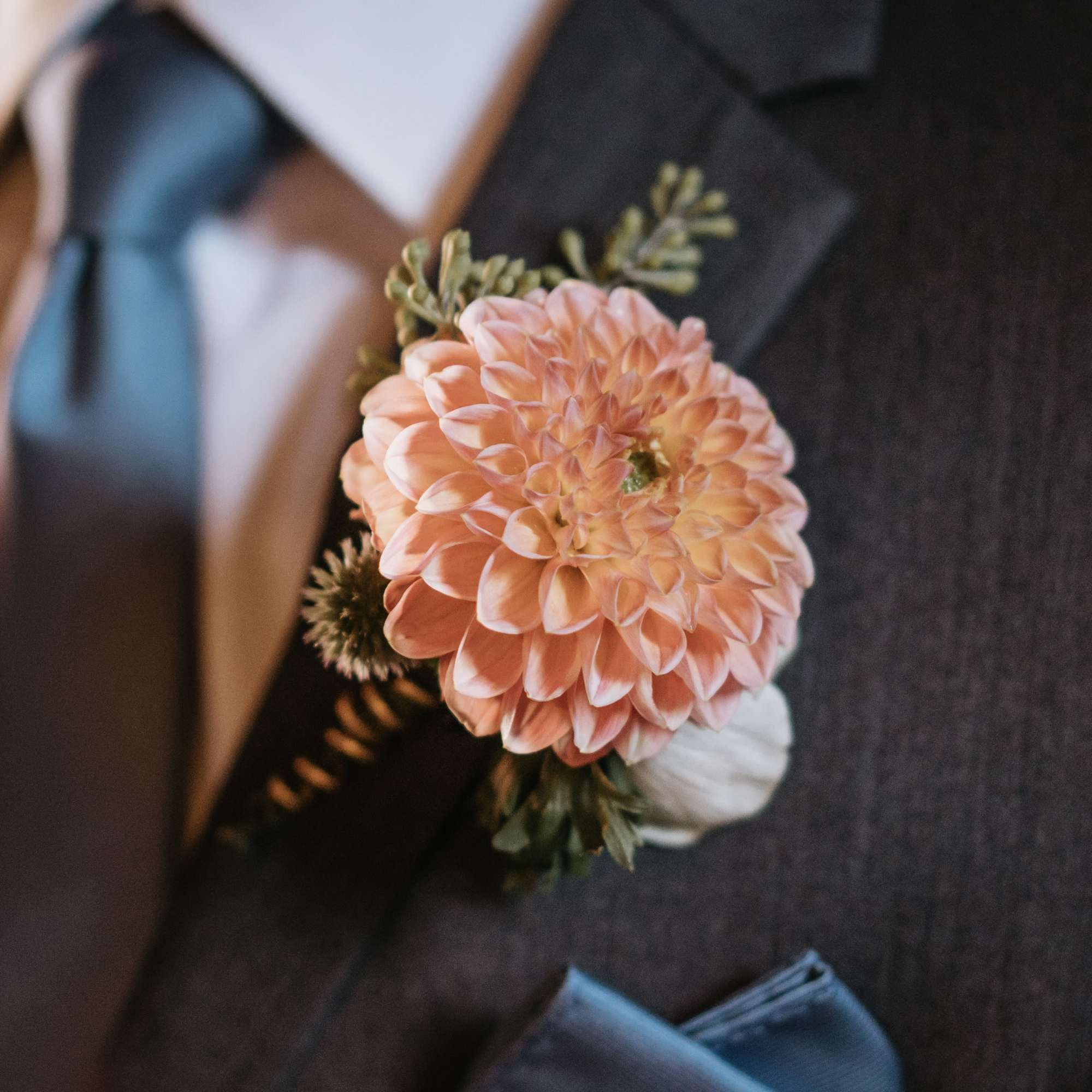 Peach dahlia boutonniere pinned to a dark suit jacket