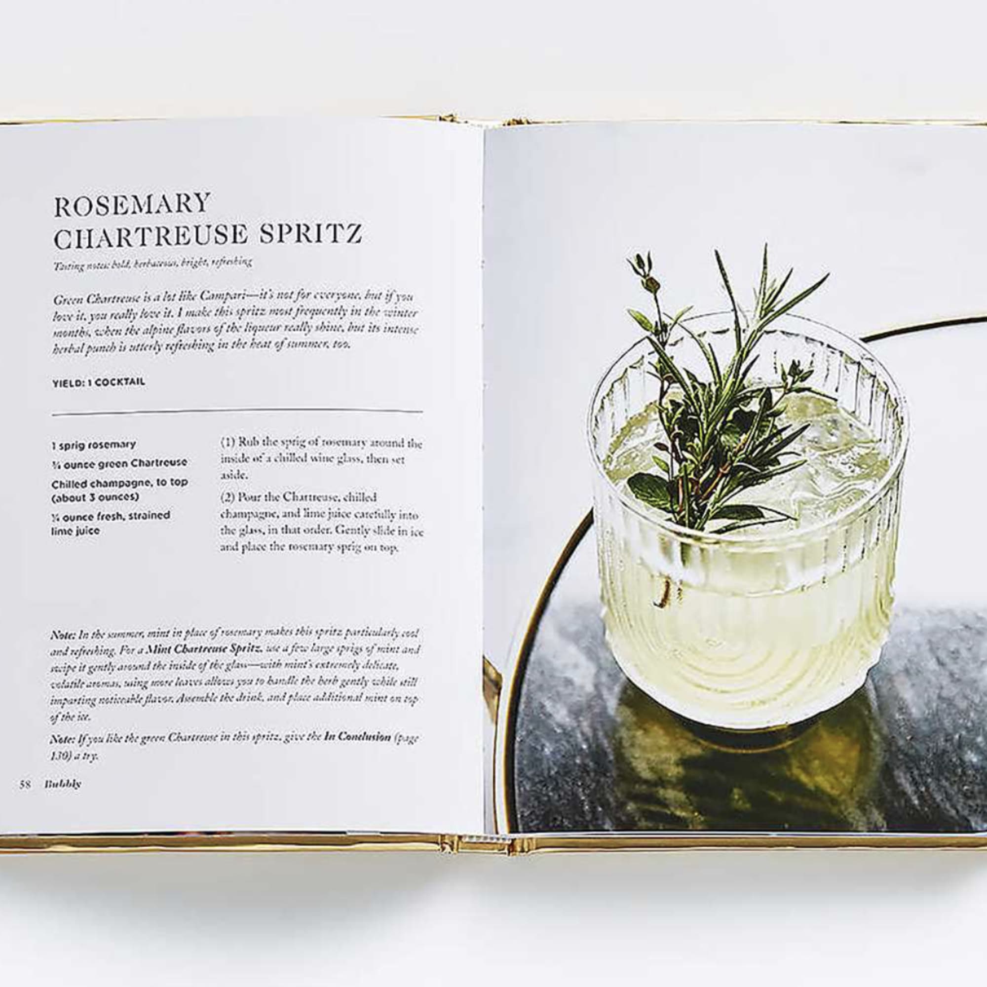 Open cookbook showing a rosemary spritz recipe and a drink in a glass