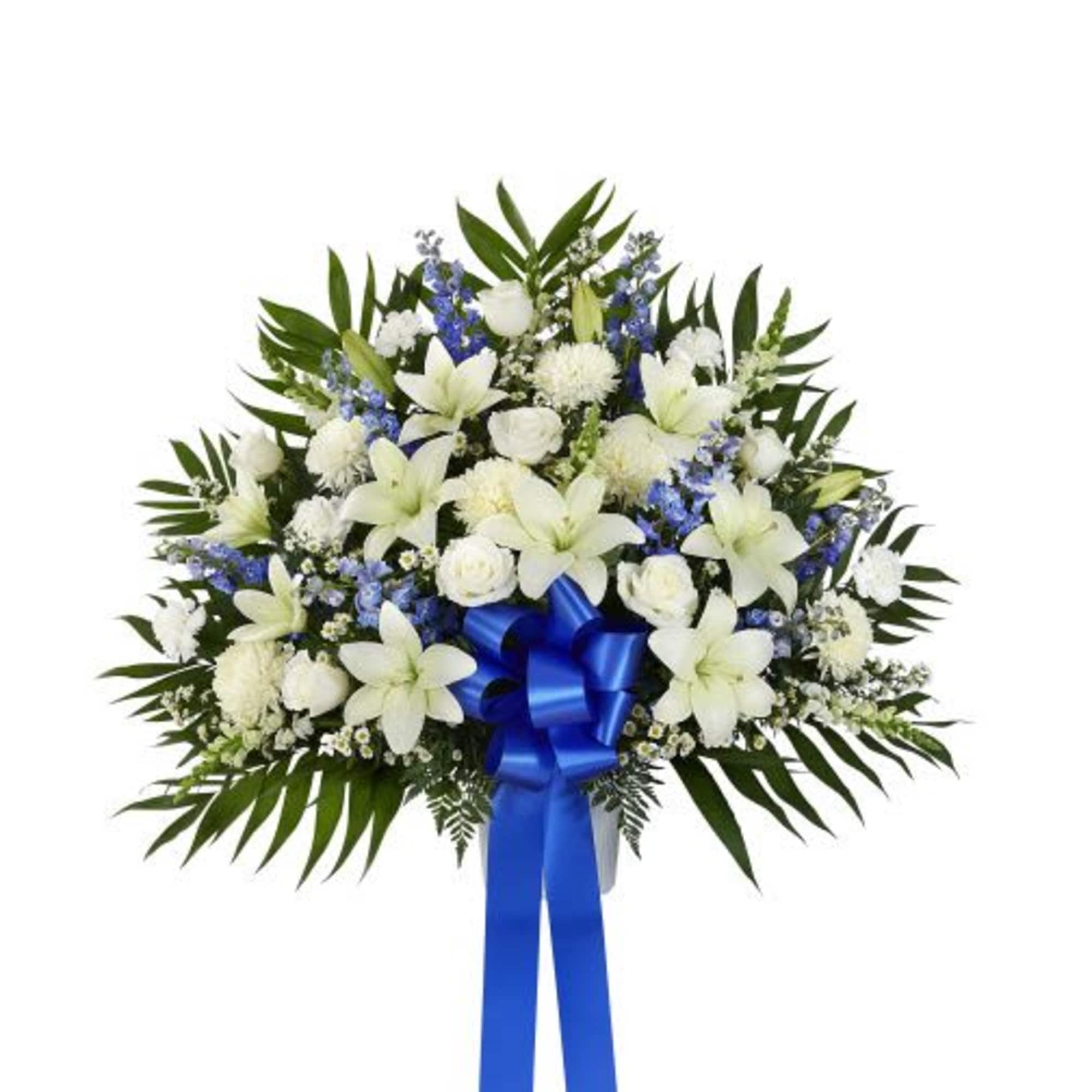 Standing spray of white lilies, roses, and carnations with blue flowers and a blue ribbon bow
