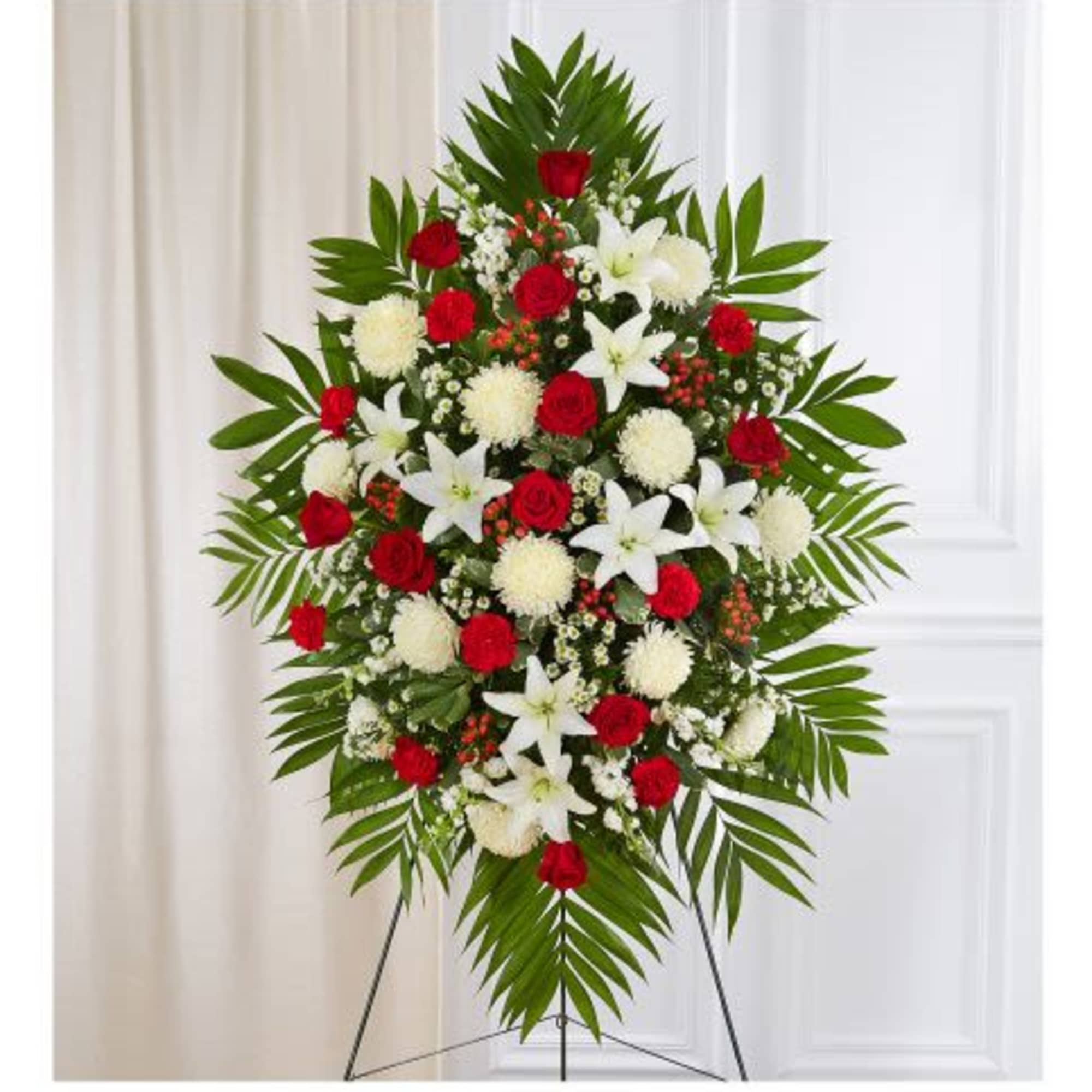 Standing spray of red roses, white lilies and mums with green palm fronds on an easel