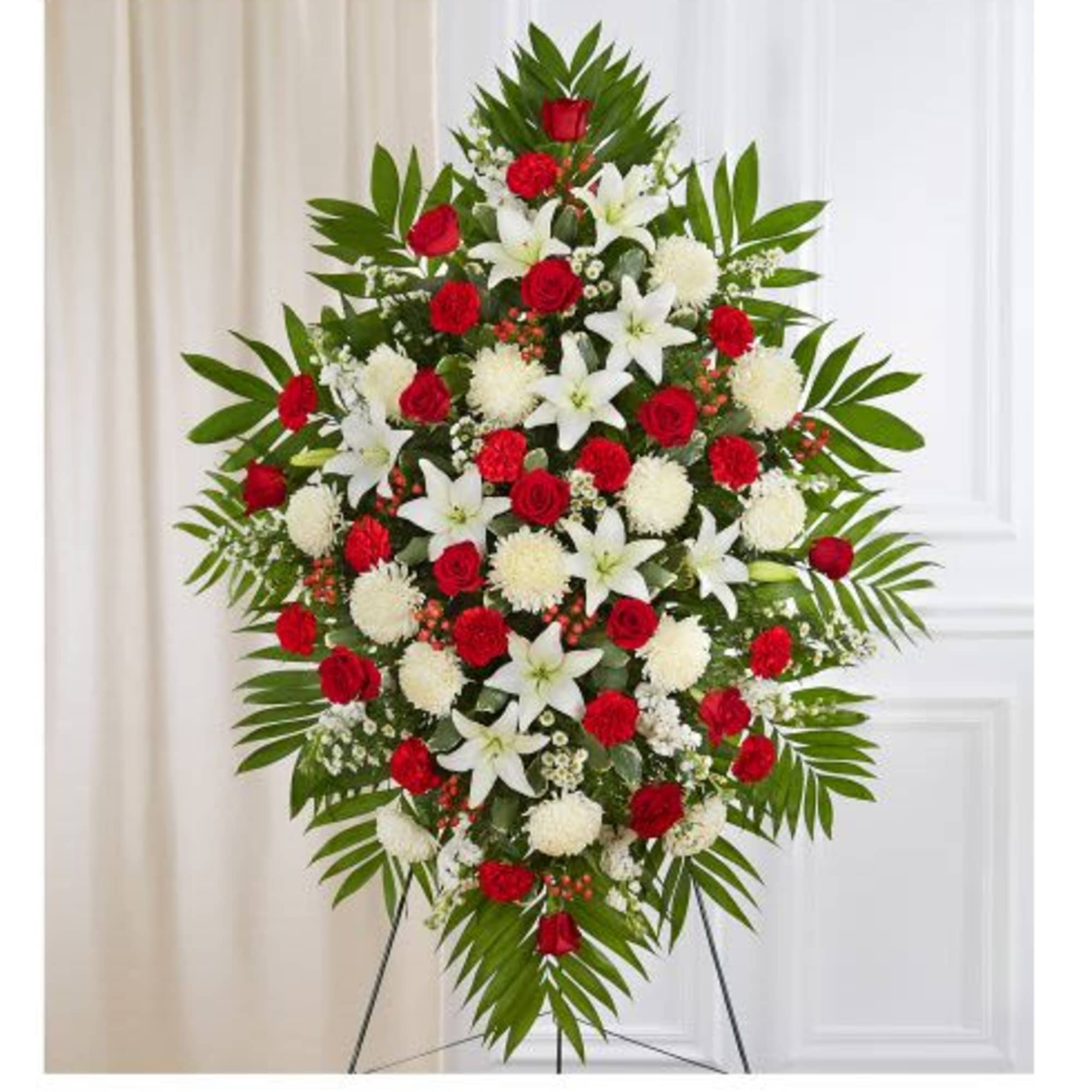 Tall red and white standing spray with lilies, roses, carnations, and mums on a metal easel.