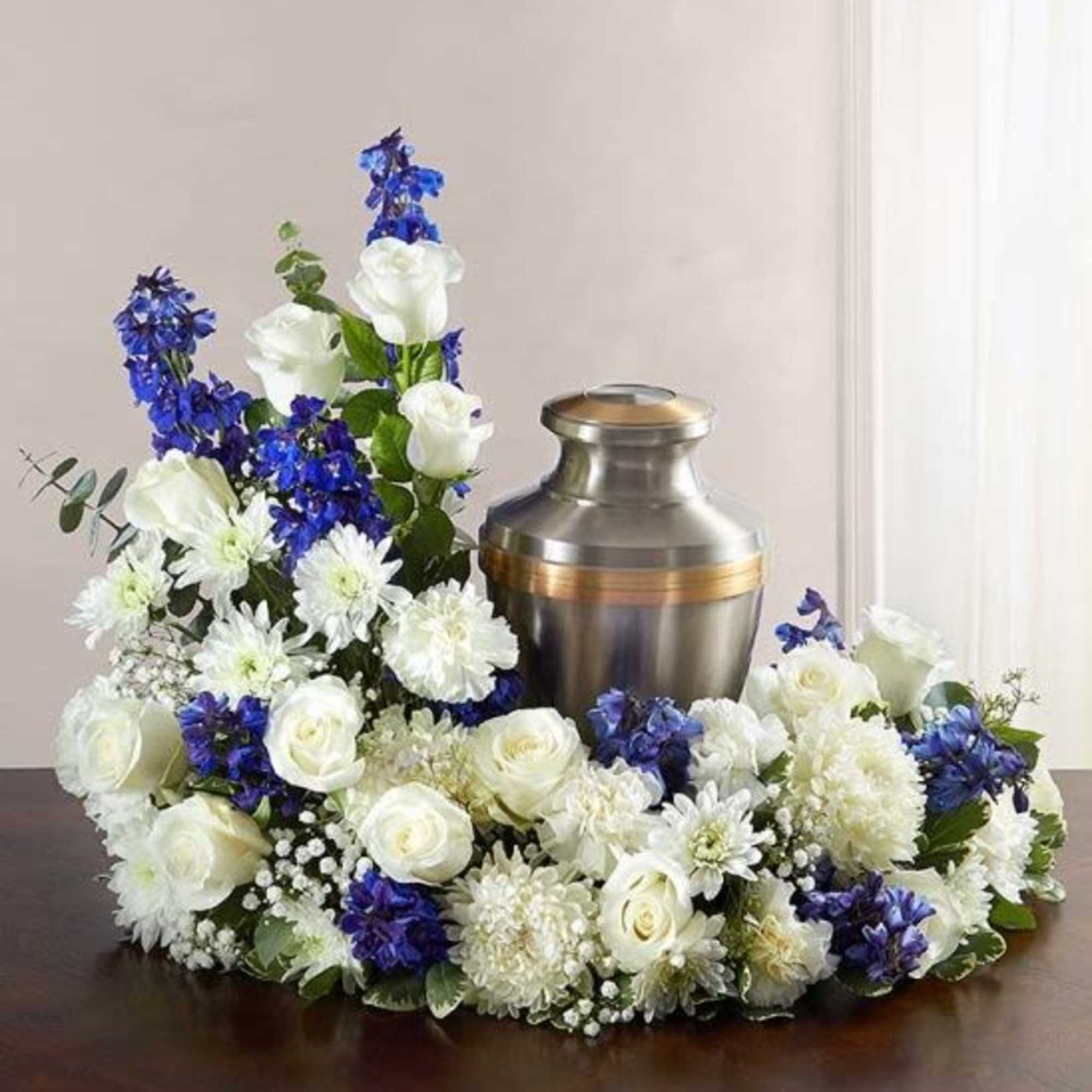 Cremation urn encircled by white and blue flowers on a wooden surface