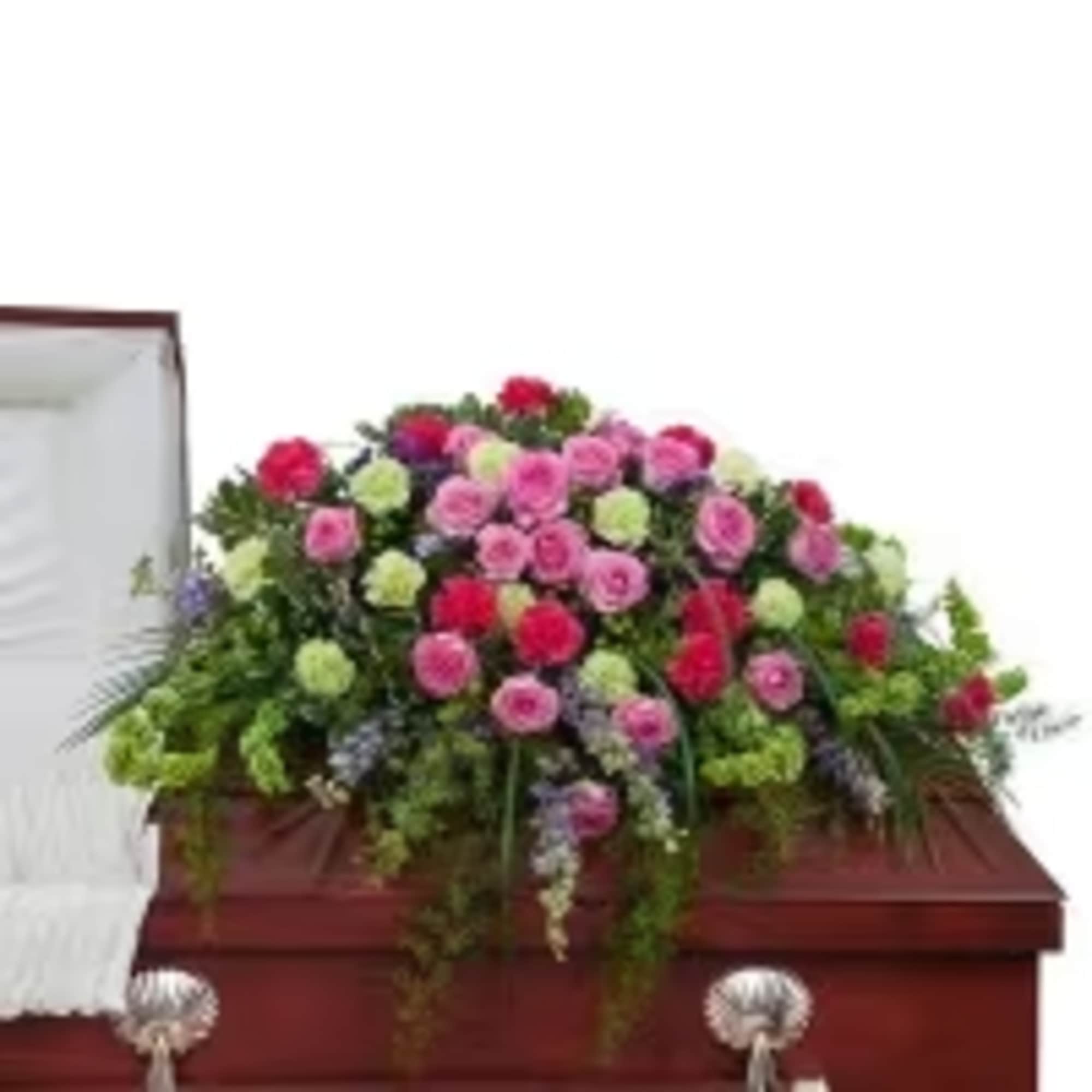 Large pink, red, and green floral casket spray on a polished wooden casket