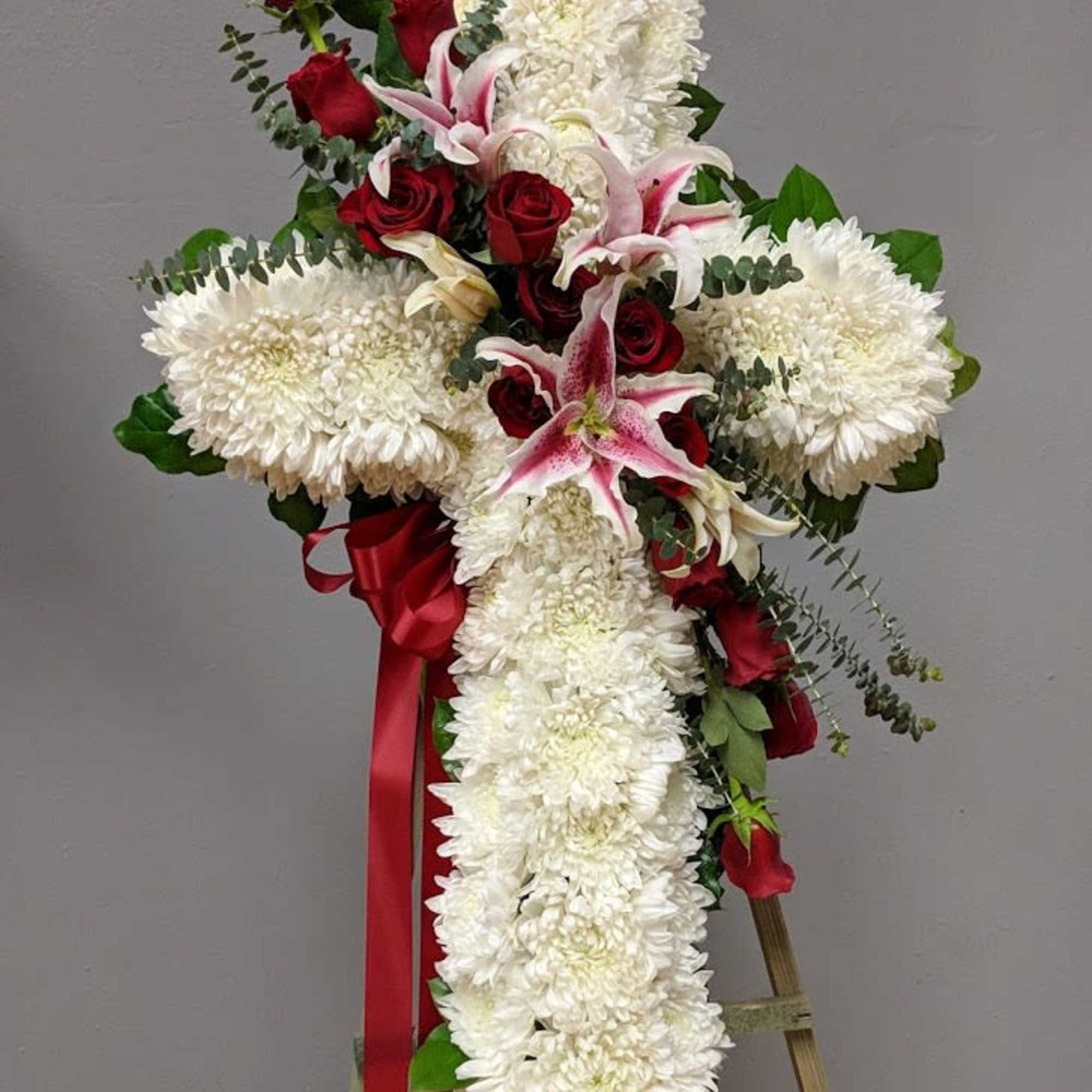 White floral cross with red roses and pink lilies on an easel