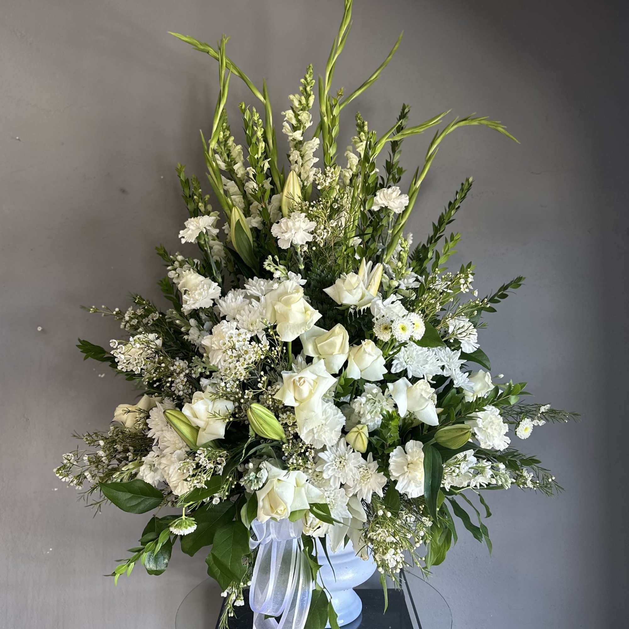 White floral arrangement in a white vase with tall greenery accents