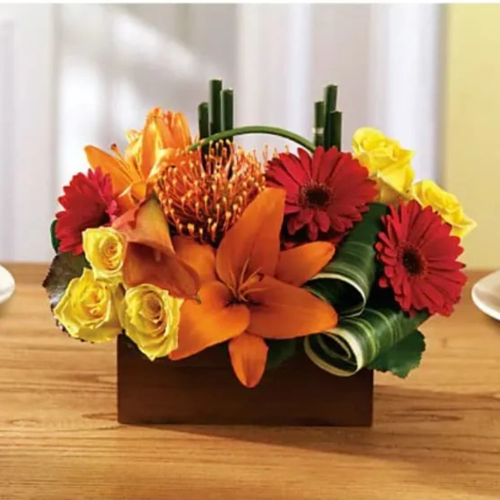 Mixed bouquet with orange lilies, red daisies, and yellow roses in a rectangular container