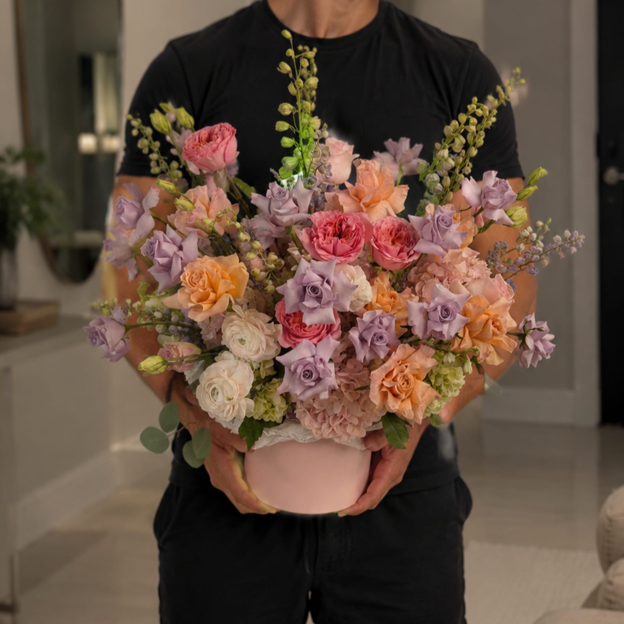 A lush, rounded pastel bouquet arranged in a pink hatbox that reads
