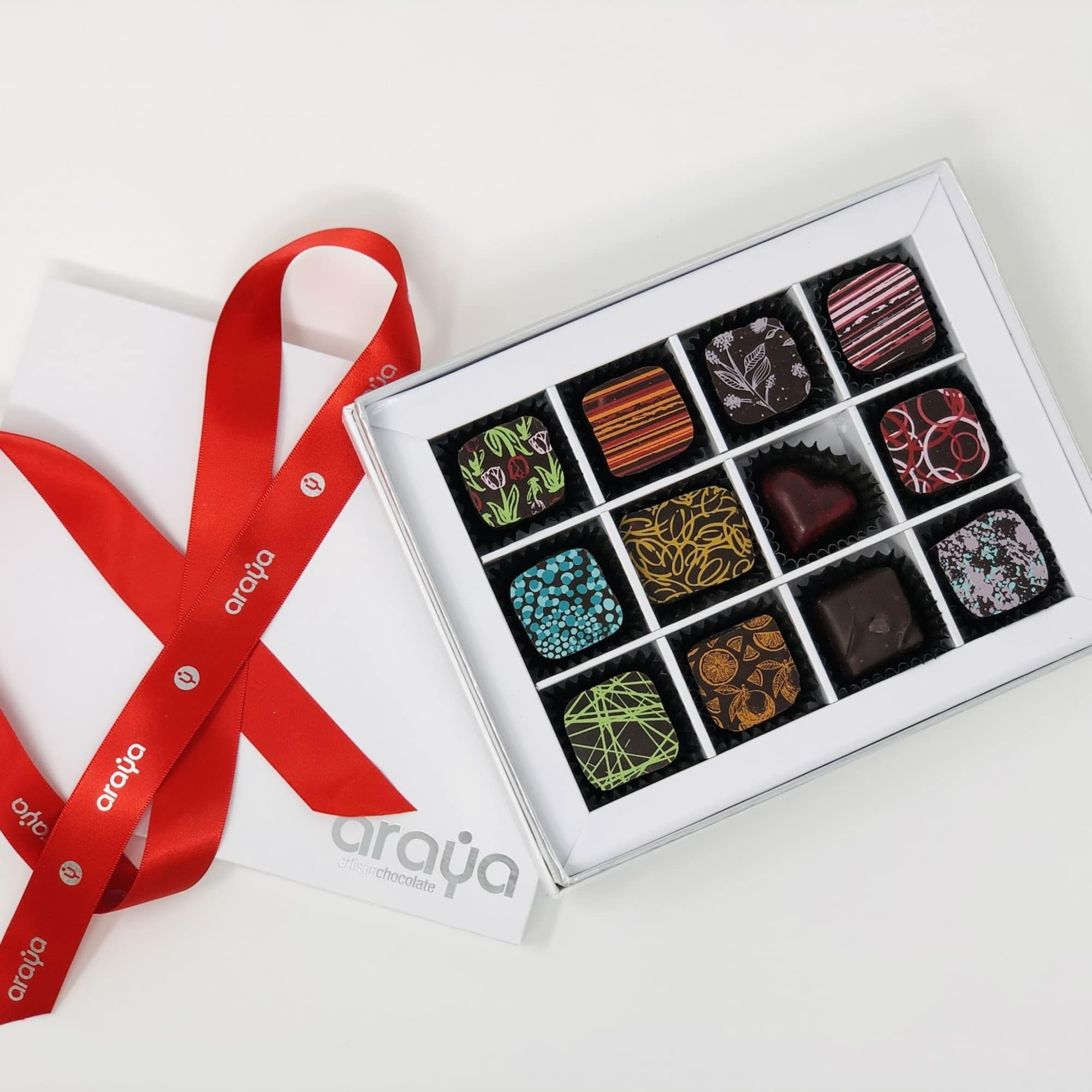 Box of assorted chocolates with a red ribbon on a white surface