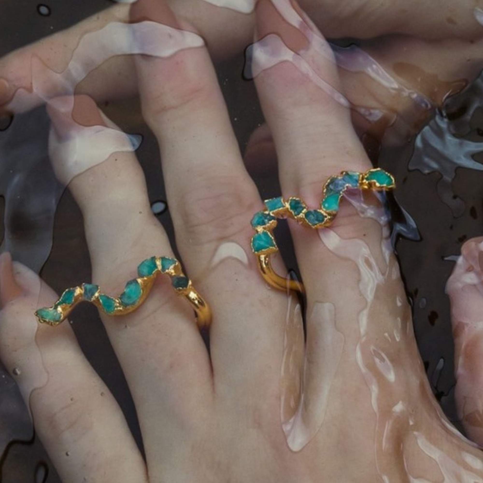 Hands wearing turquoise stone rings submerged in water