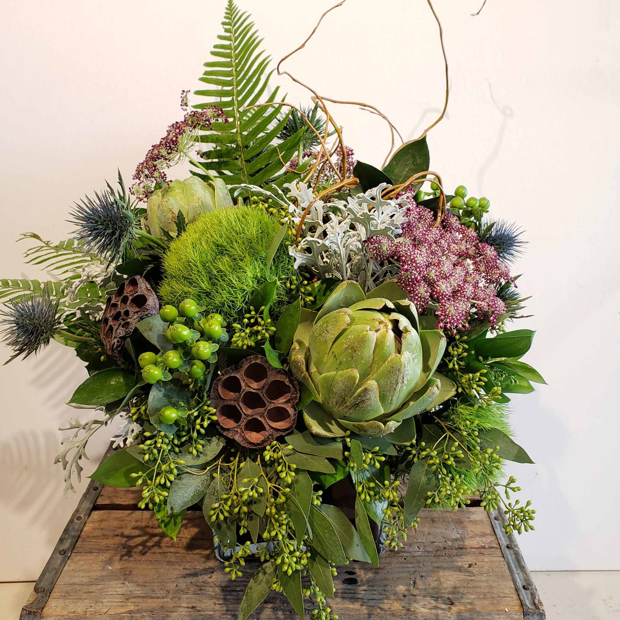 Green floral arrangement with artichokes, berries, and dried pods