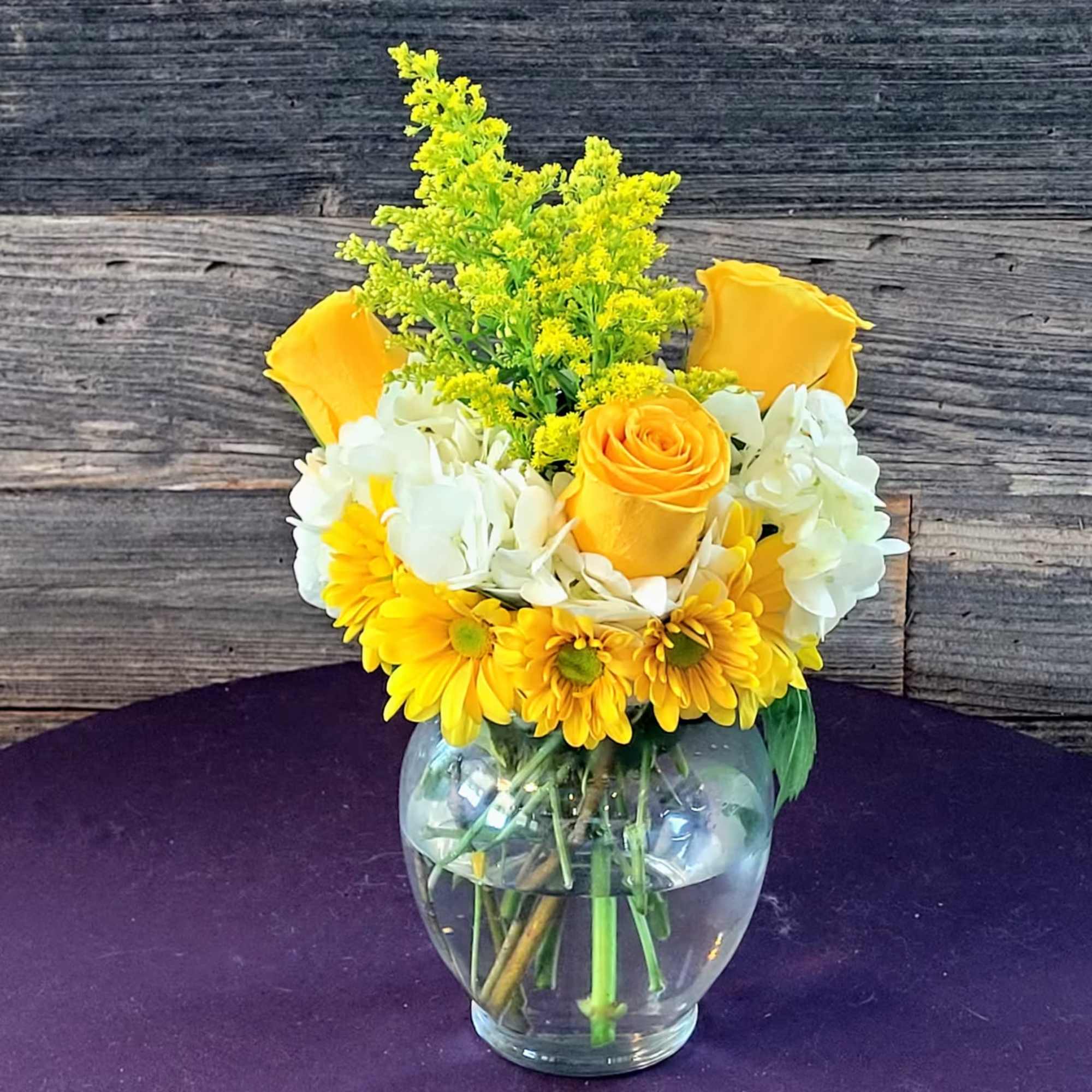 Yellow roses and daisies arranged in a clear glass vase.