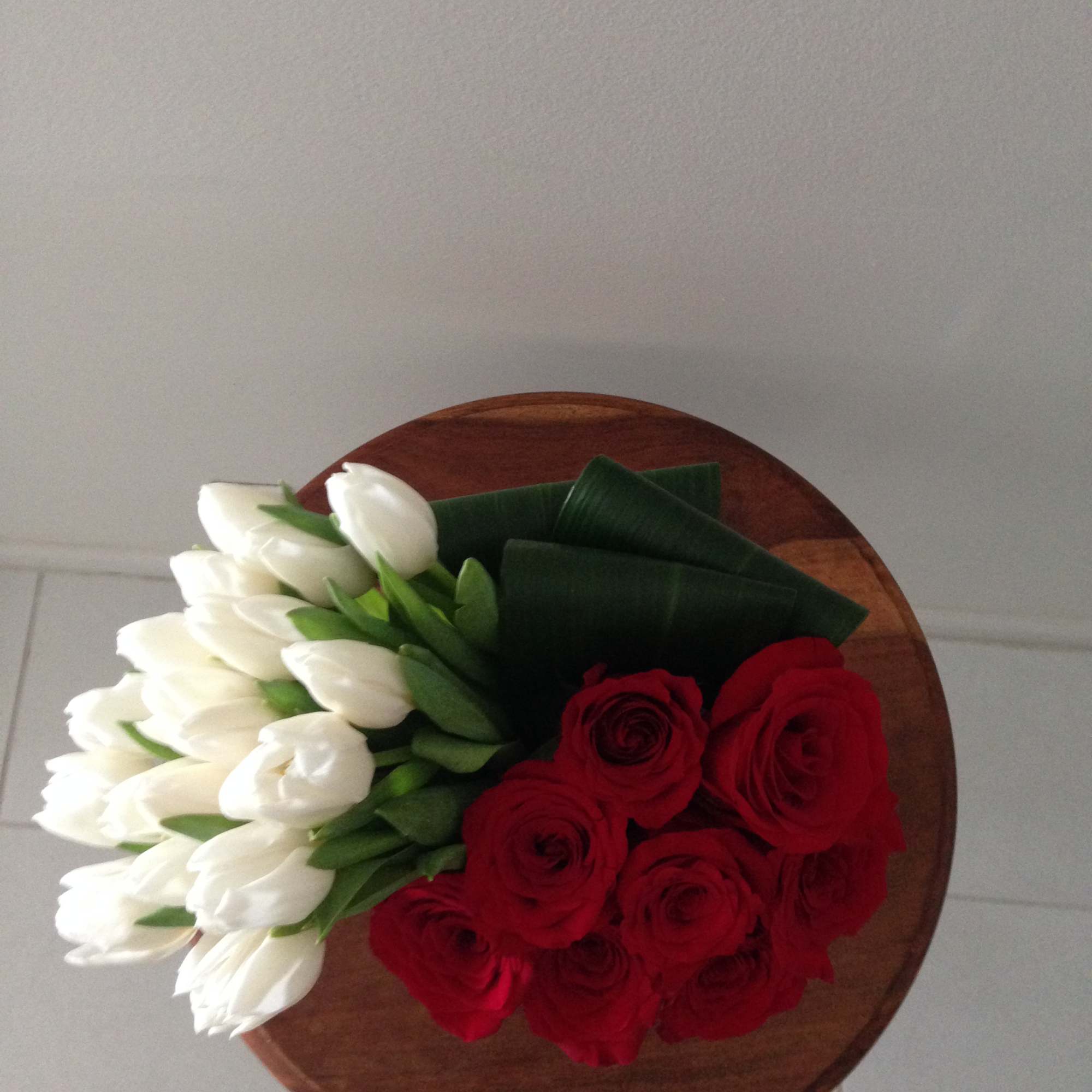 Bouquet of red roses and white tulips on a round wooden surface