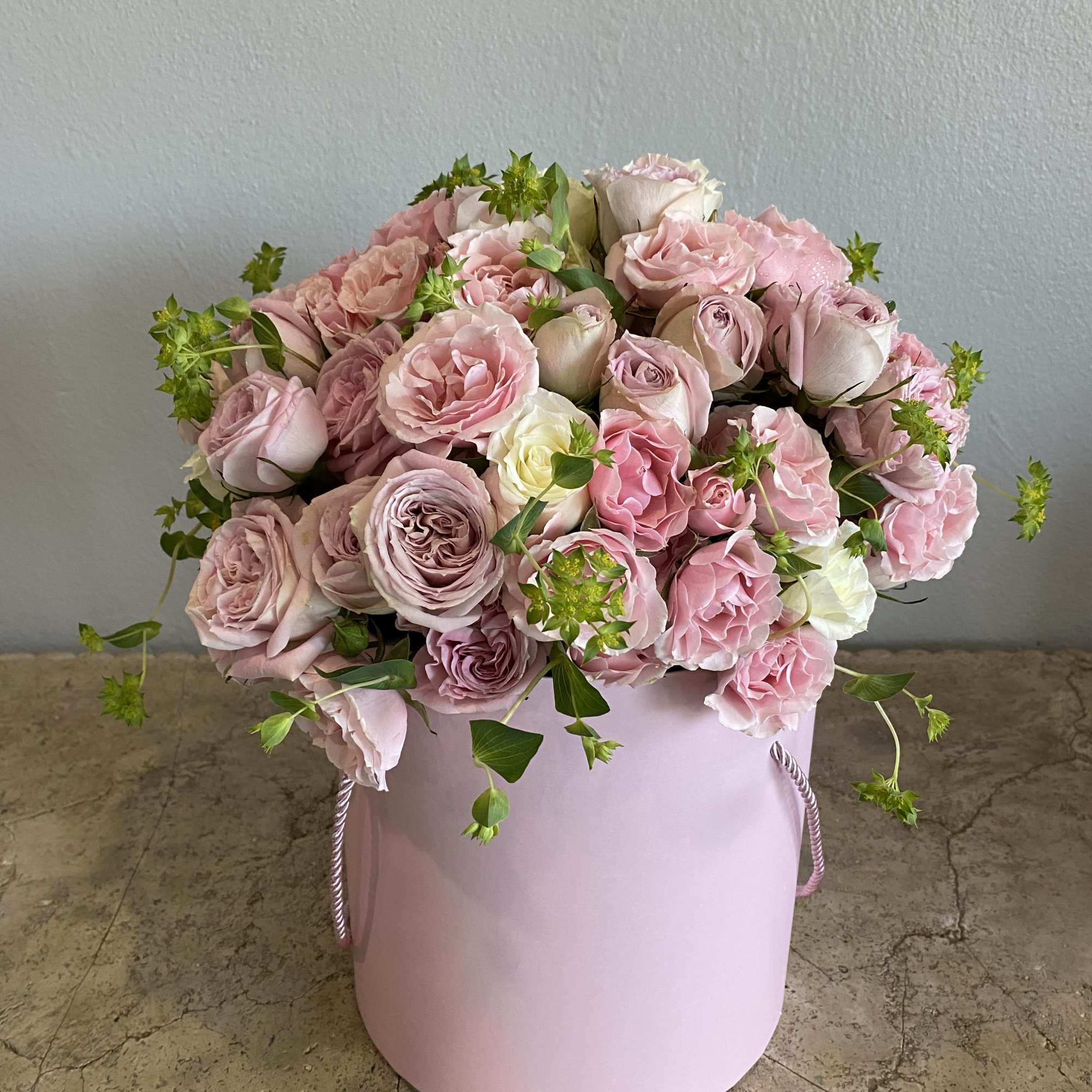 Pink roses and carnations arranged in a pale pink hat box