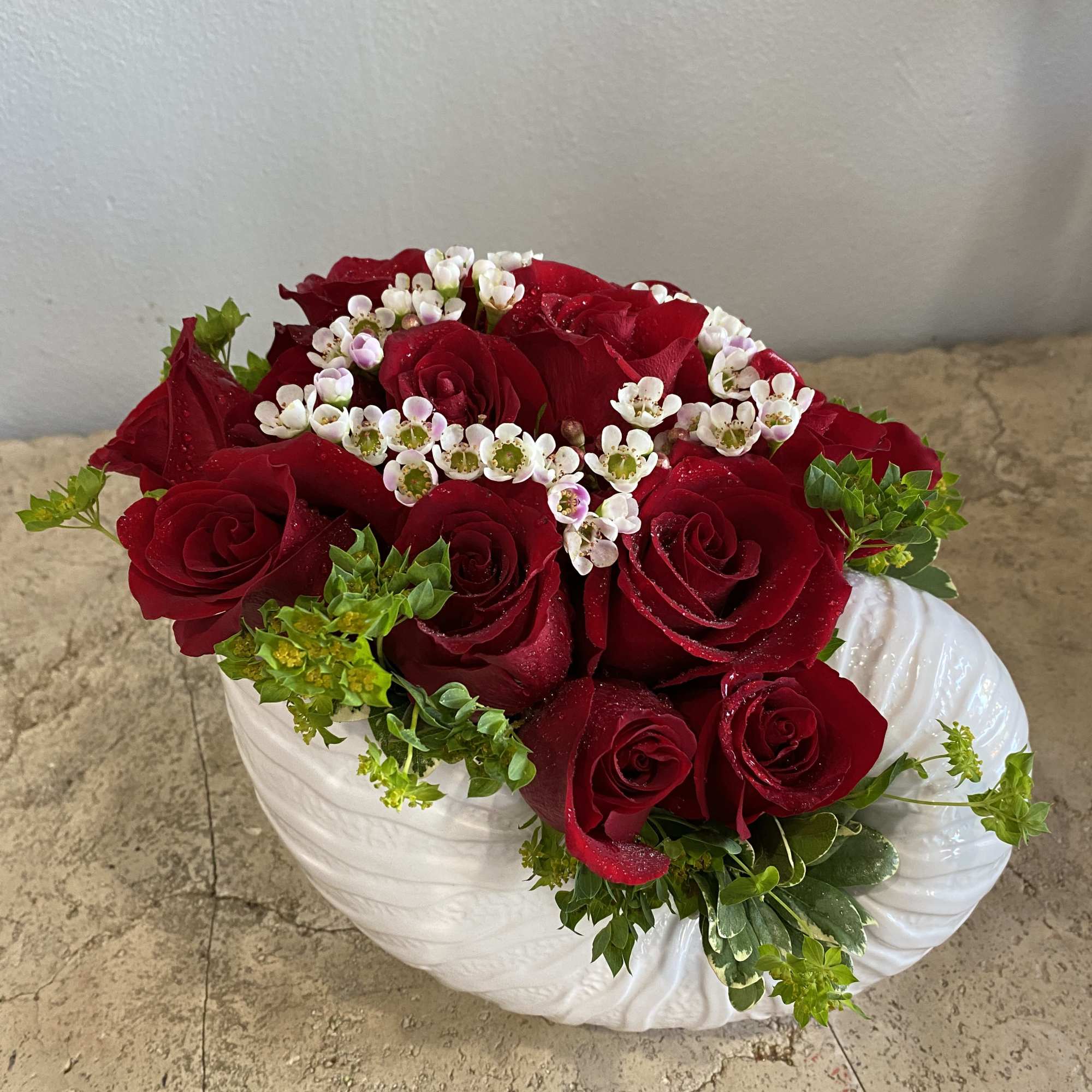 Red roses arranged in a white ceramic vase with small white filler flowers
