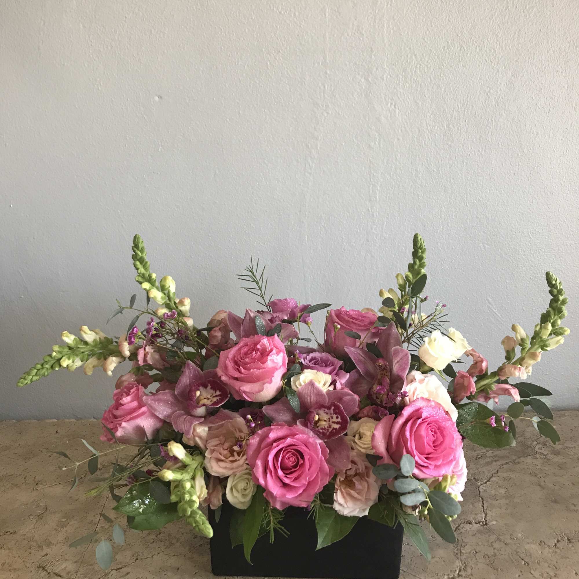 Pink rose and orchid arrangement in a black rectangular container