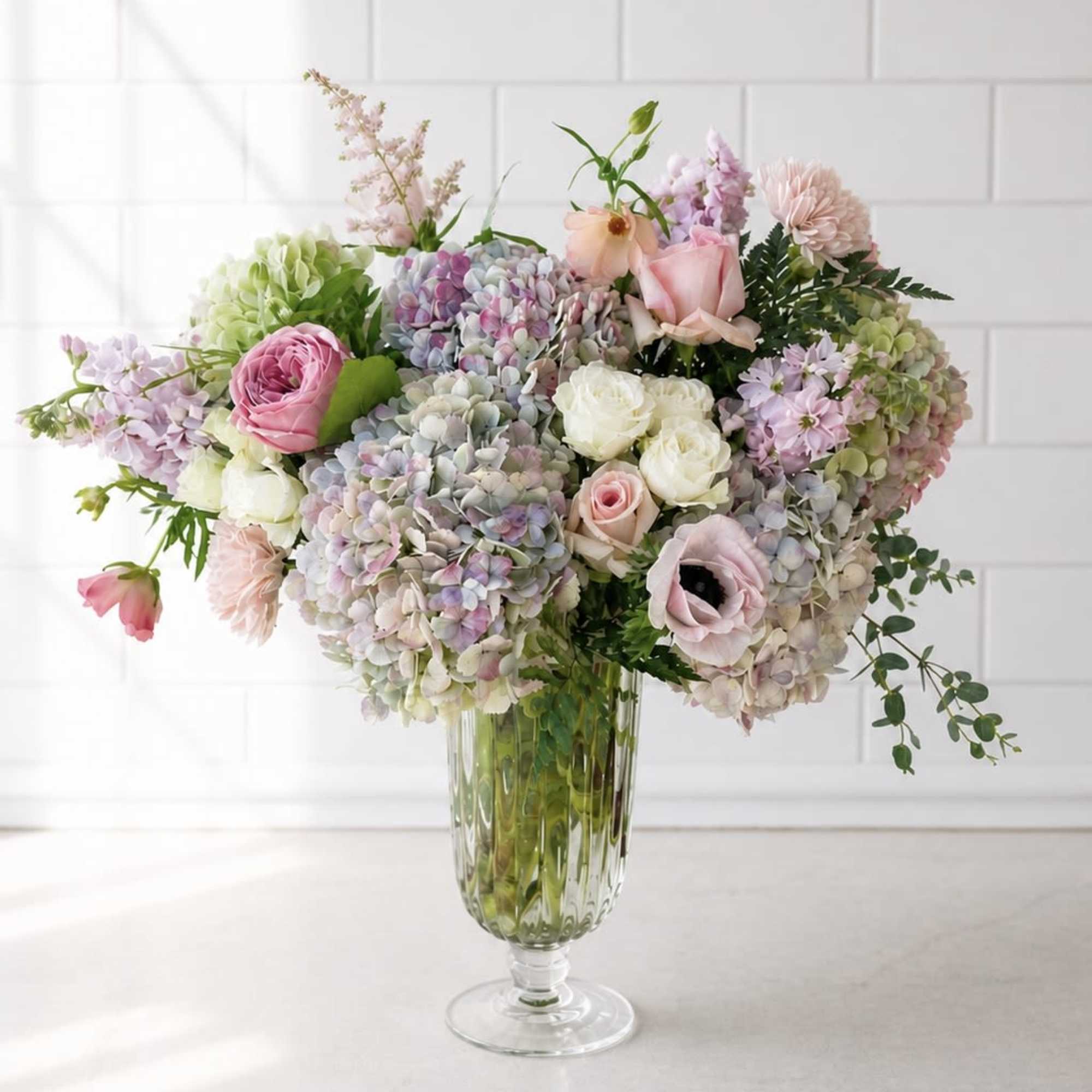 Pastel bouquet of hydrangeas, roses, and anemones in a clear glass vase