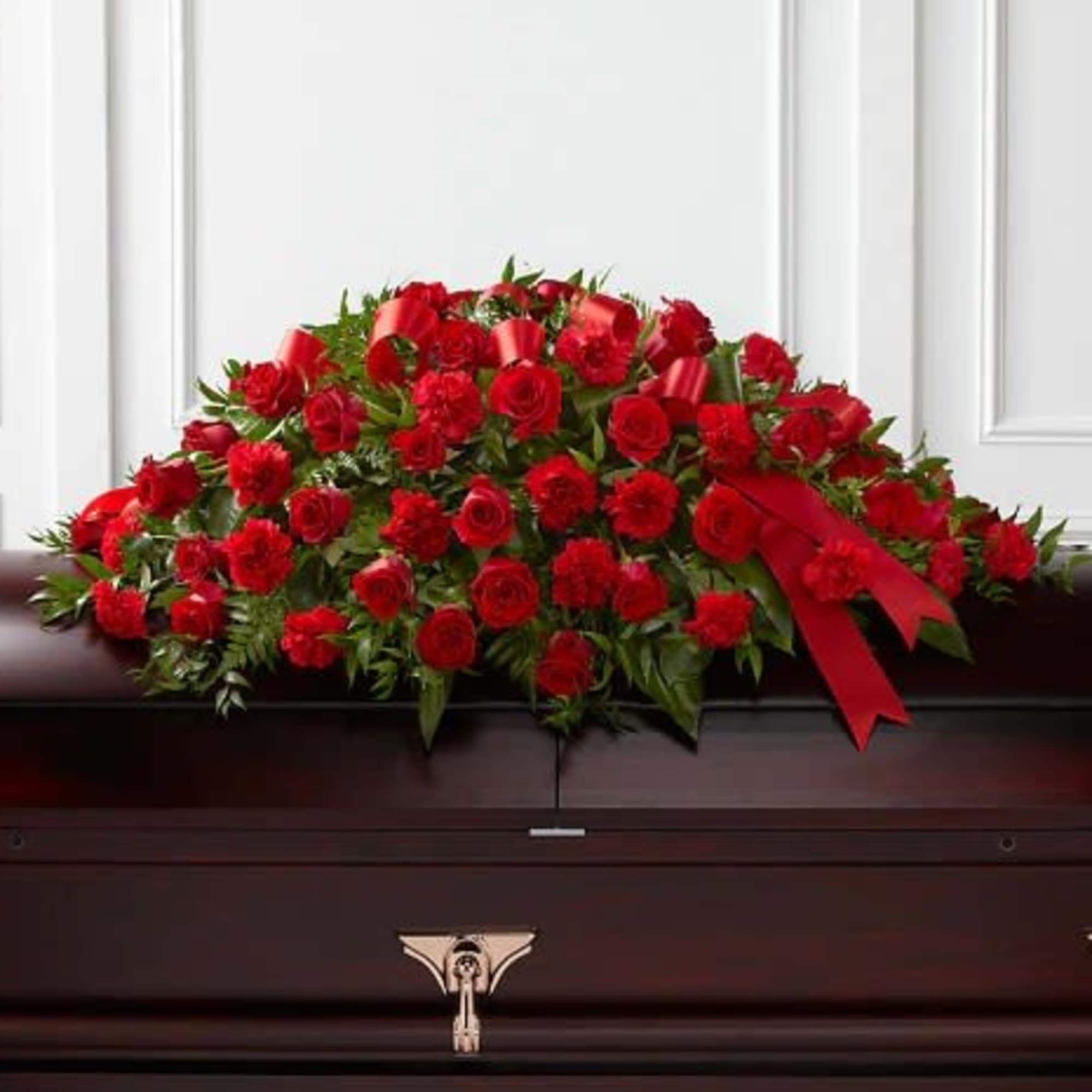 Red rose casket spray with a ribbon on a dark casket