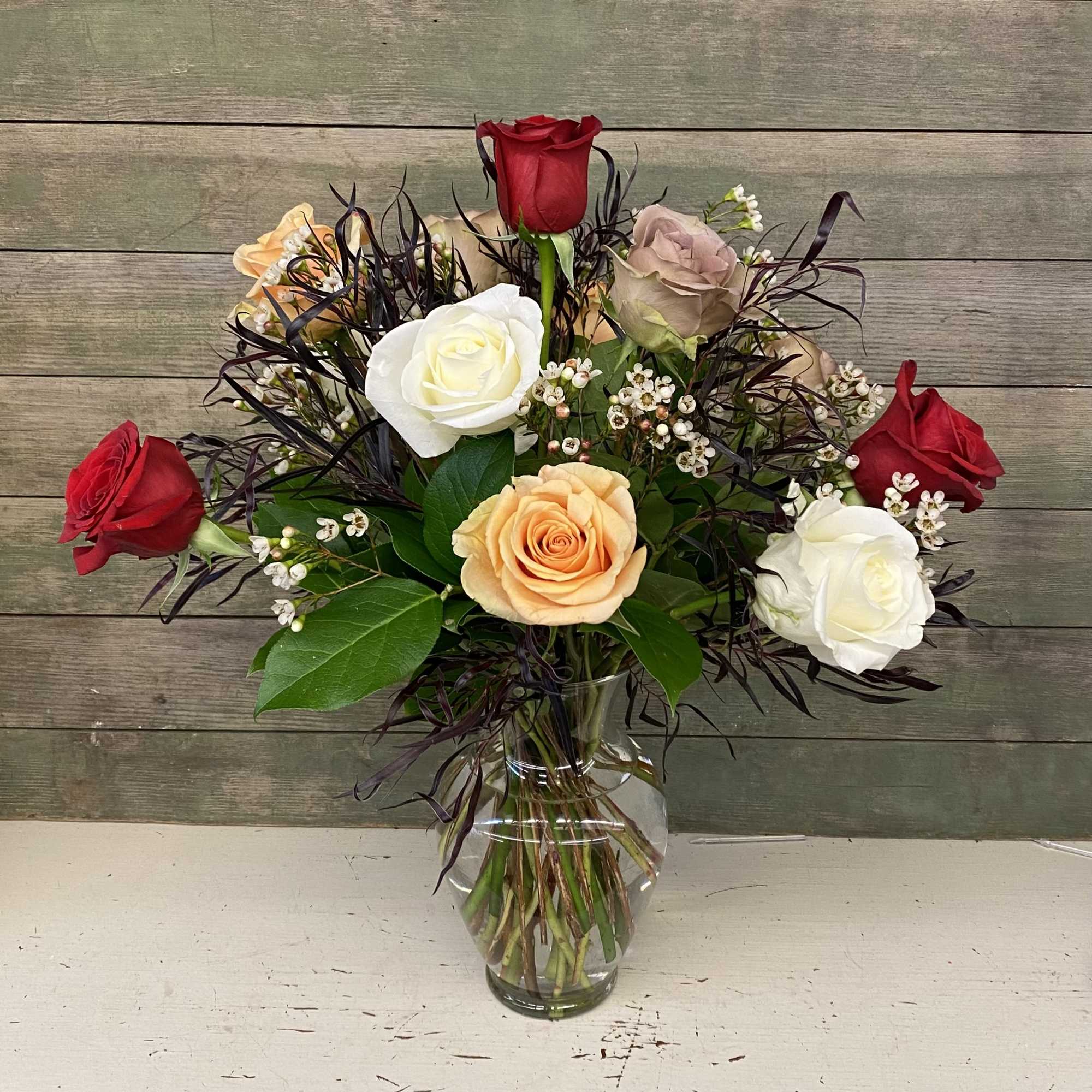 Bouquet of red, white, peach, and blush roses in a clear glass vase