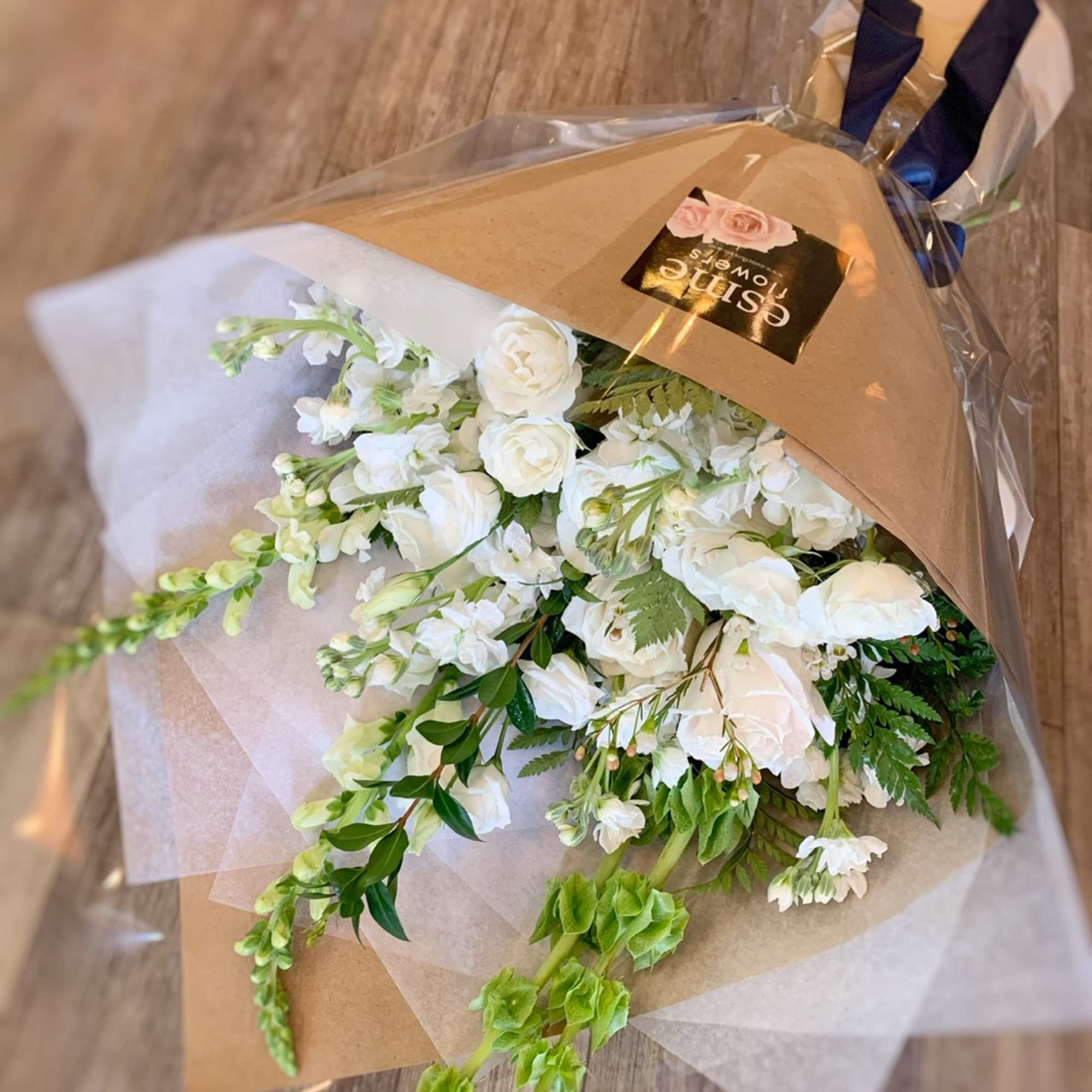 Wrapped bouquet of white flowers with green accents on a wooden floor