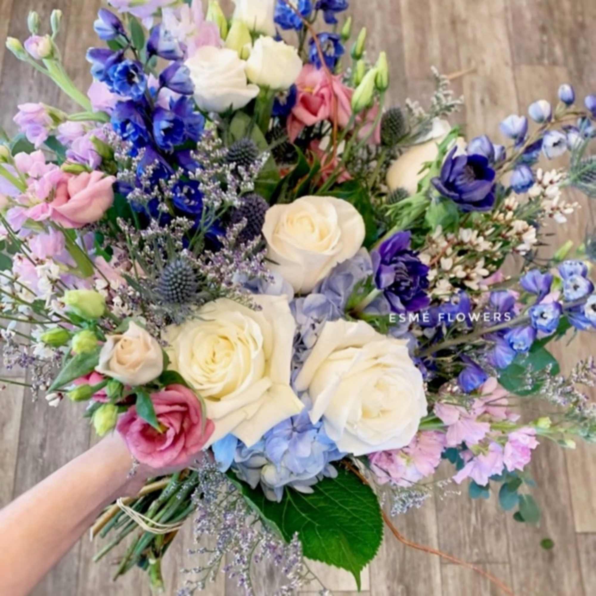 Handheld bouquet of white roses, blue flowers, and pink blooms