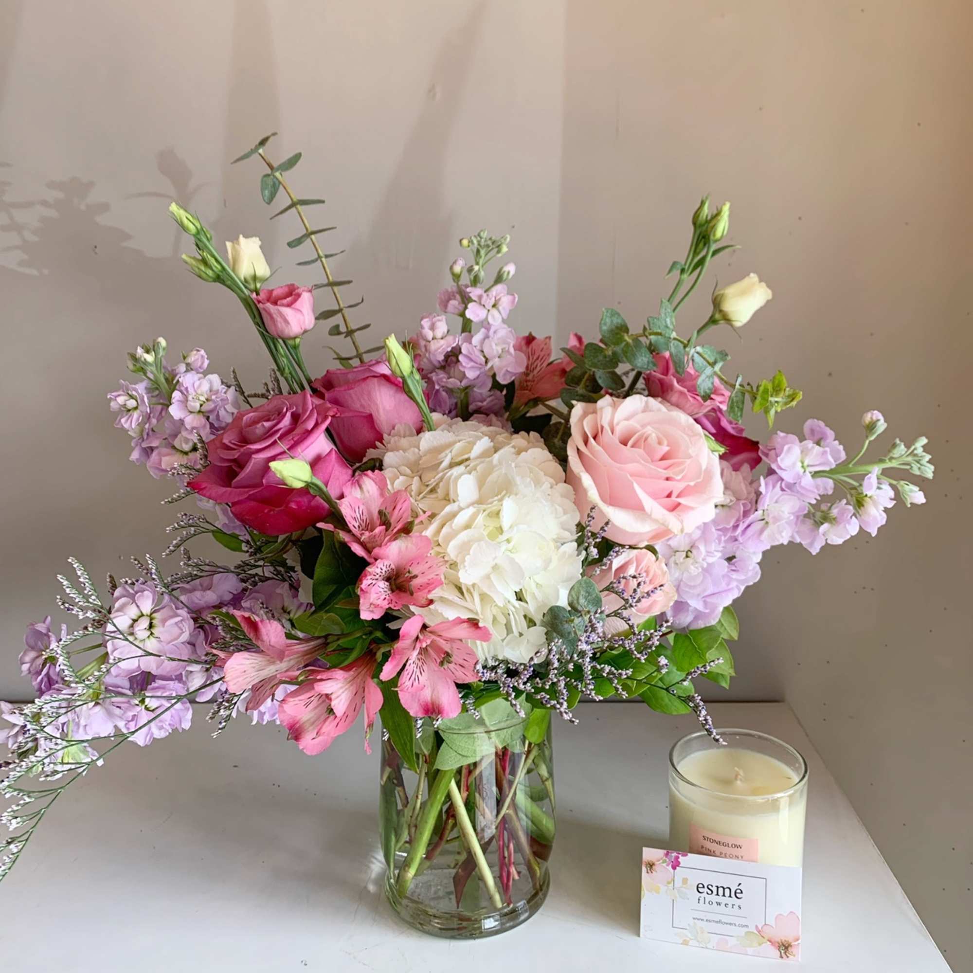 Pink and white mixed flower bouquet in a glass vase beside a candle