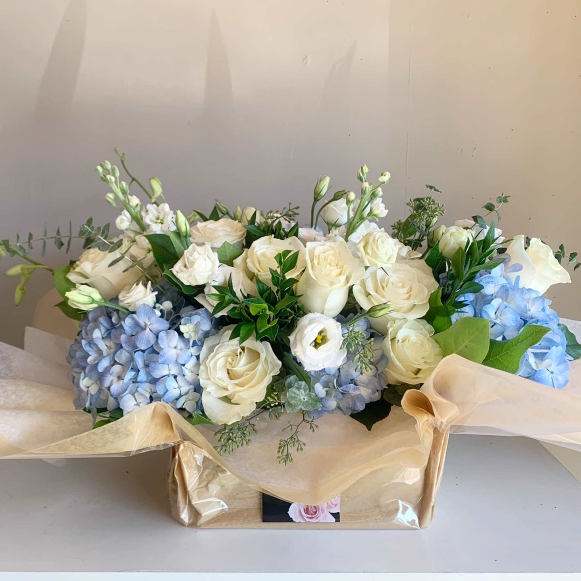 White roses and blue hydrangeas arranged in a gift box with sheer ribbon
