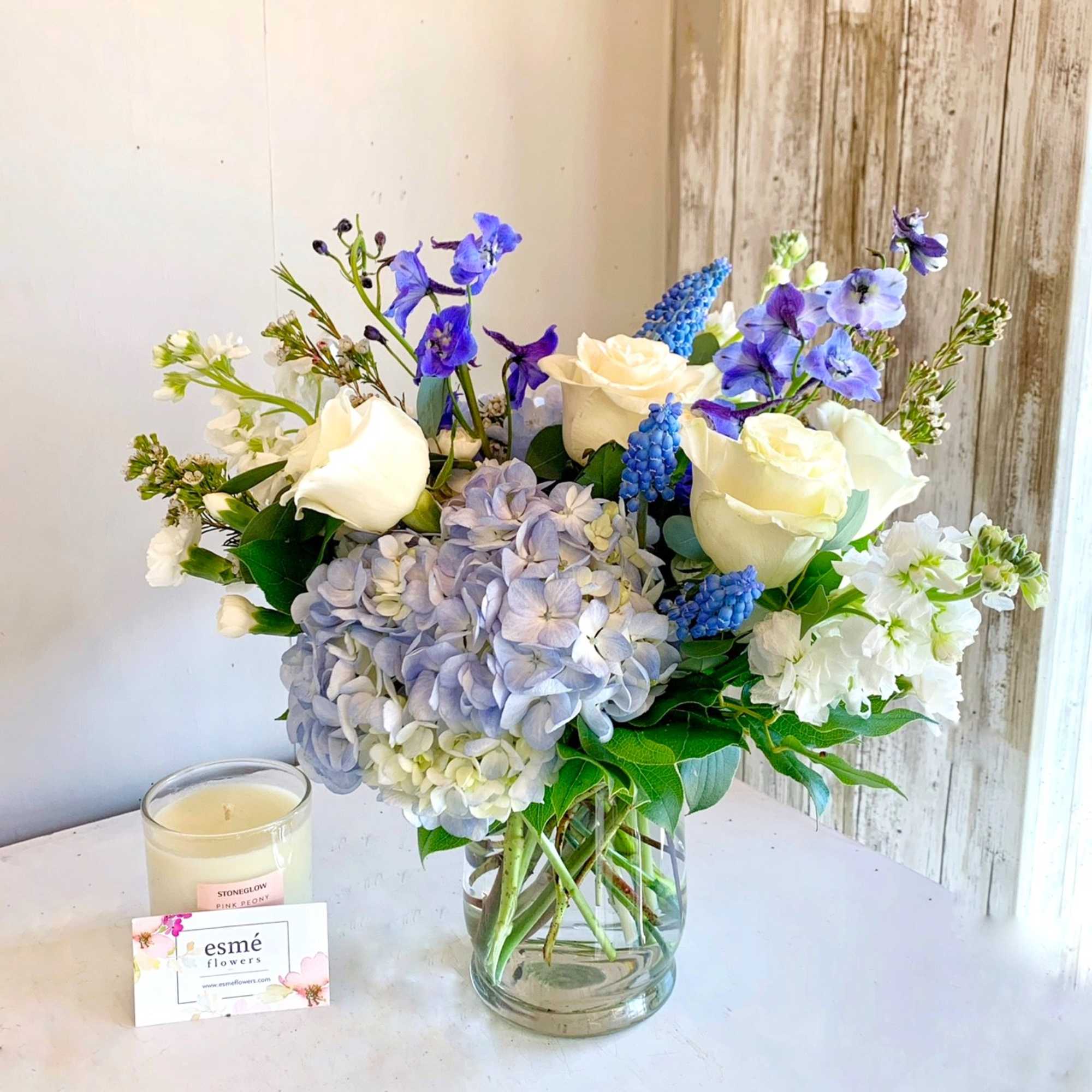 Bouquet of white roses, blue flowers, and pale hydrangeas in a glass vase