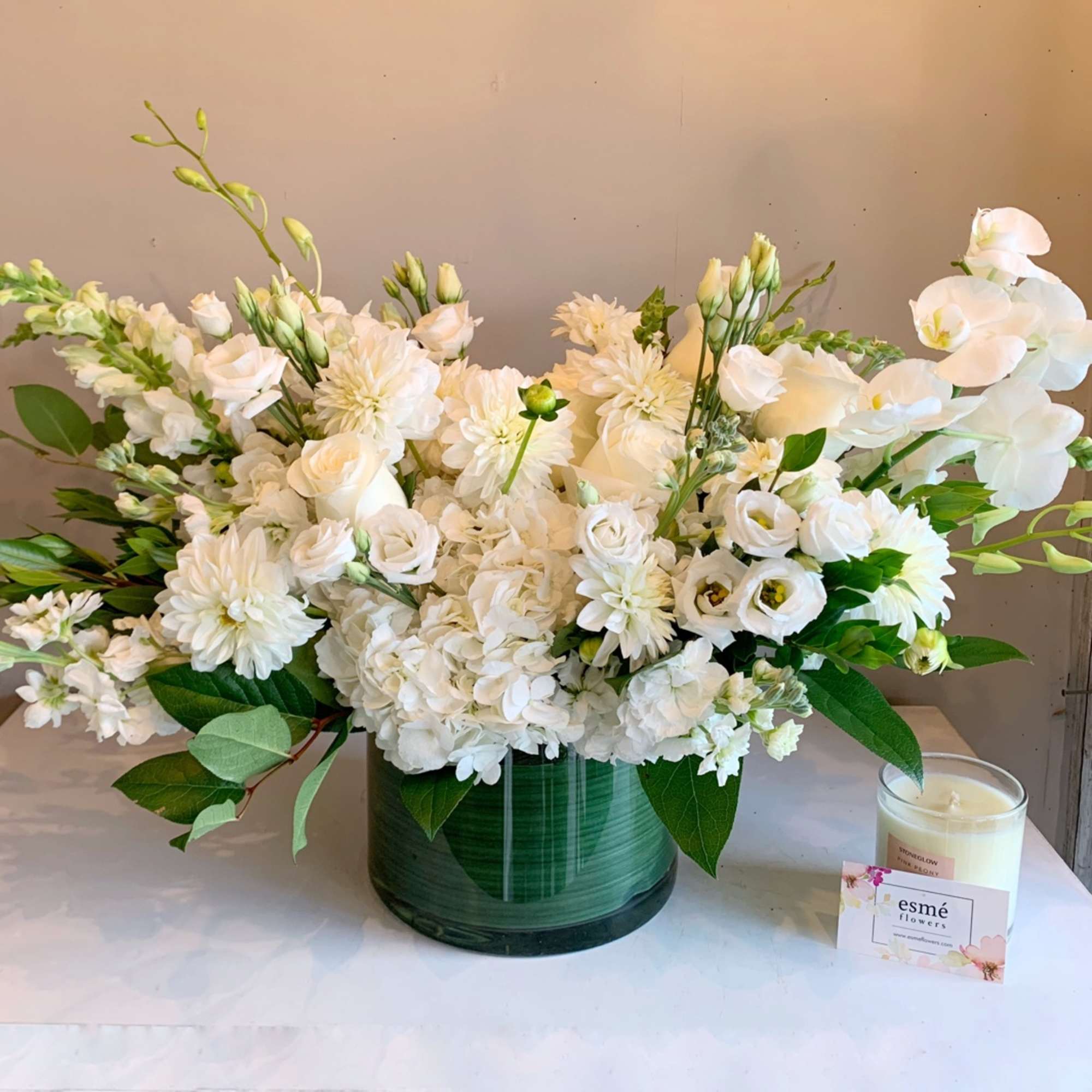 White floral arrangement in a green vase with a candle beside it