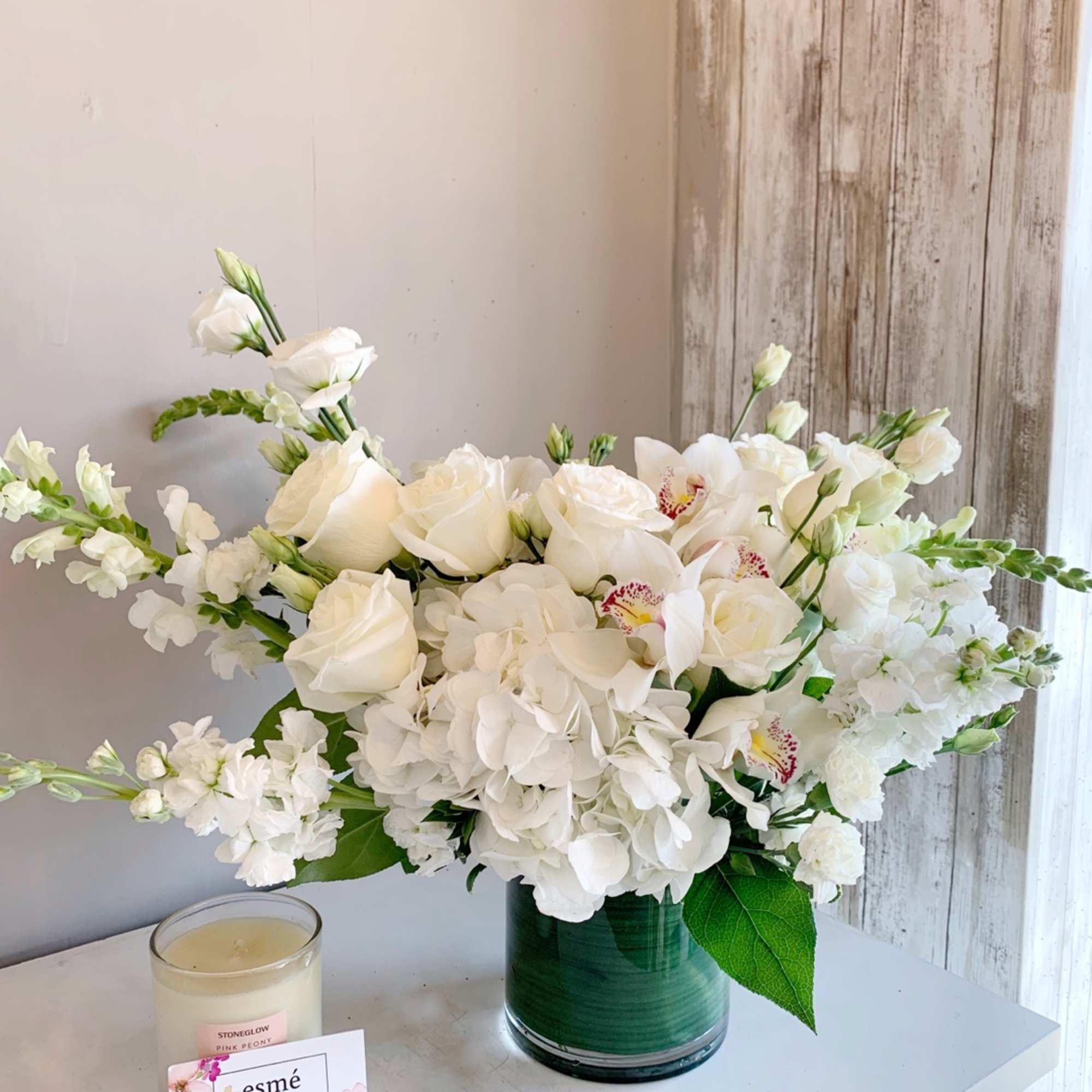 White floral arrangement in a green glass vase with a candle beside it