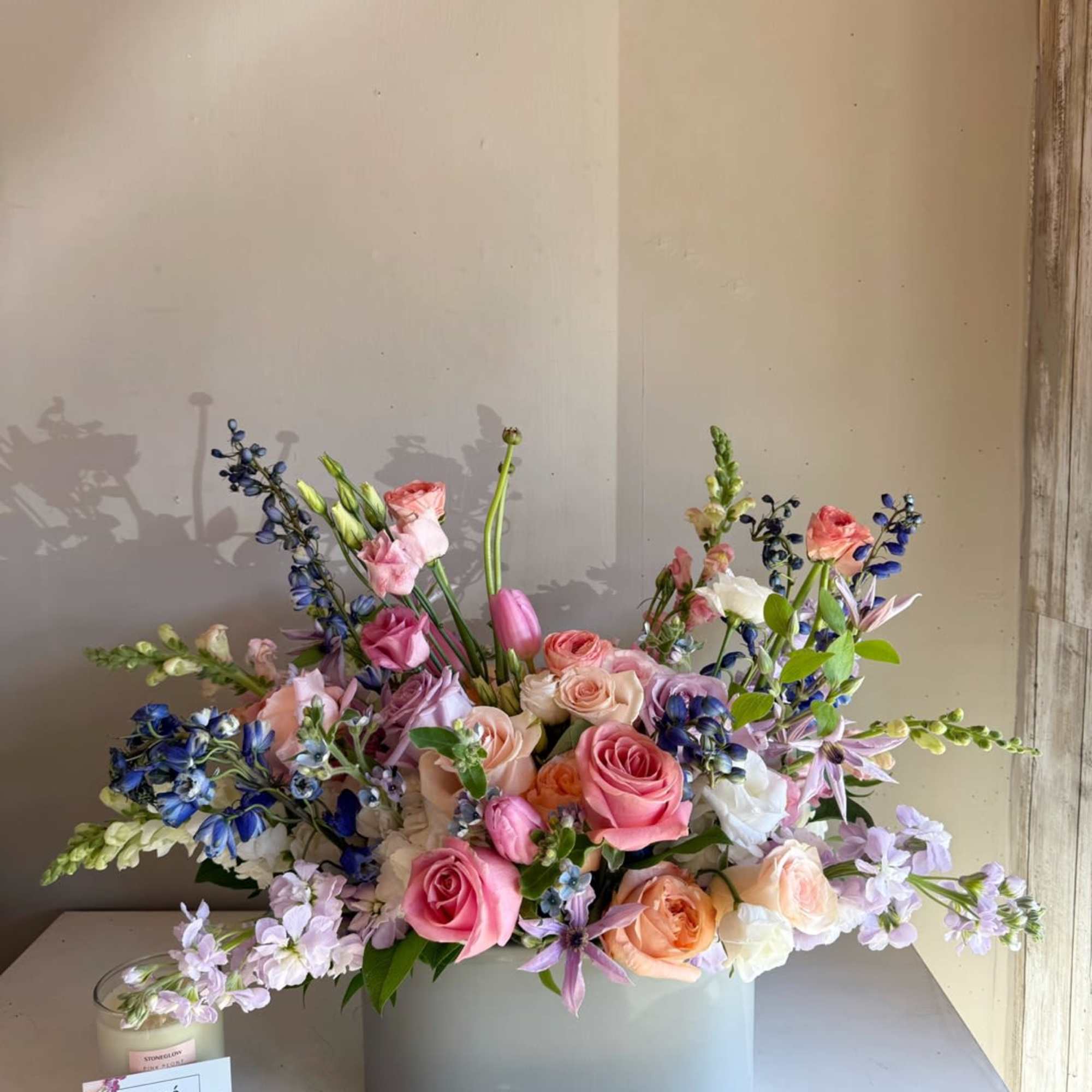 Pastel bouquet of roses, tulips, and blue flowers in a gray vase
