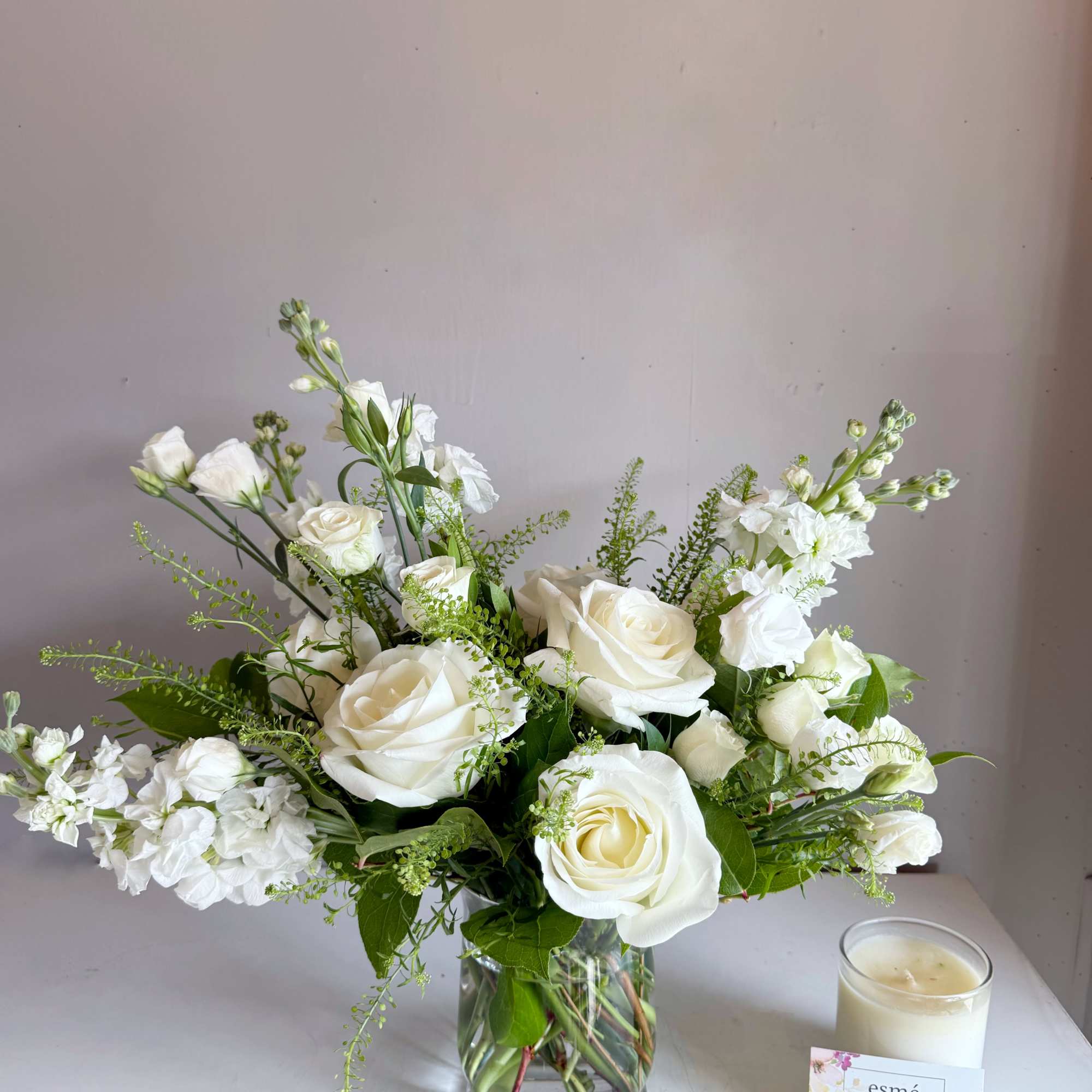 White roses and white filler flowers arranged in a clear glass vase.