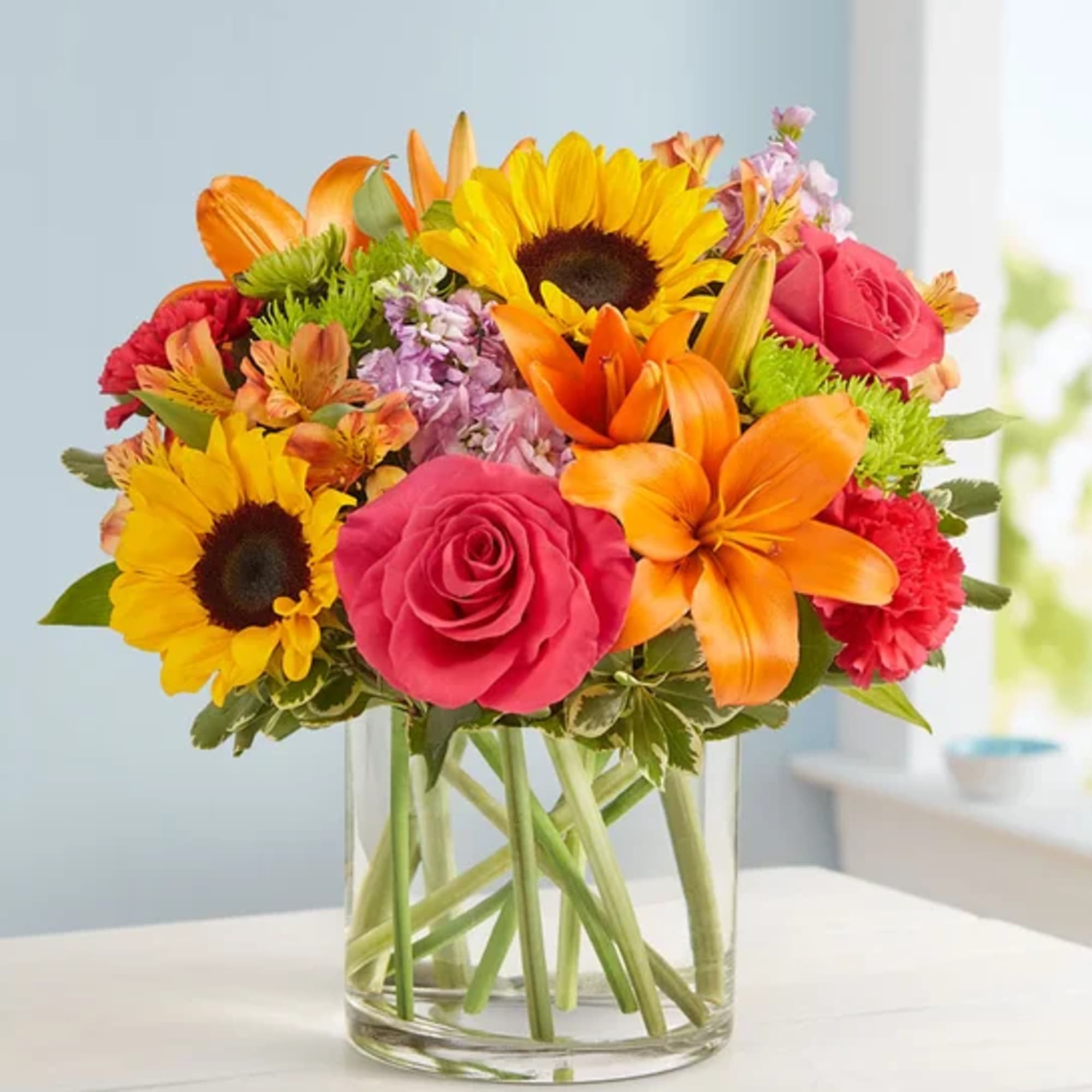 Bright mixed bouquet with sunflowers, roses, lilies, and carnations in a glass vase