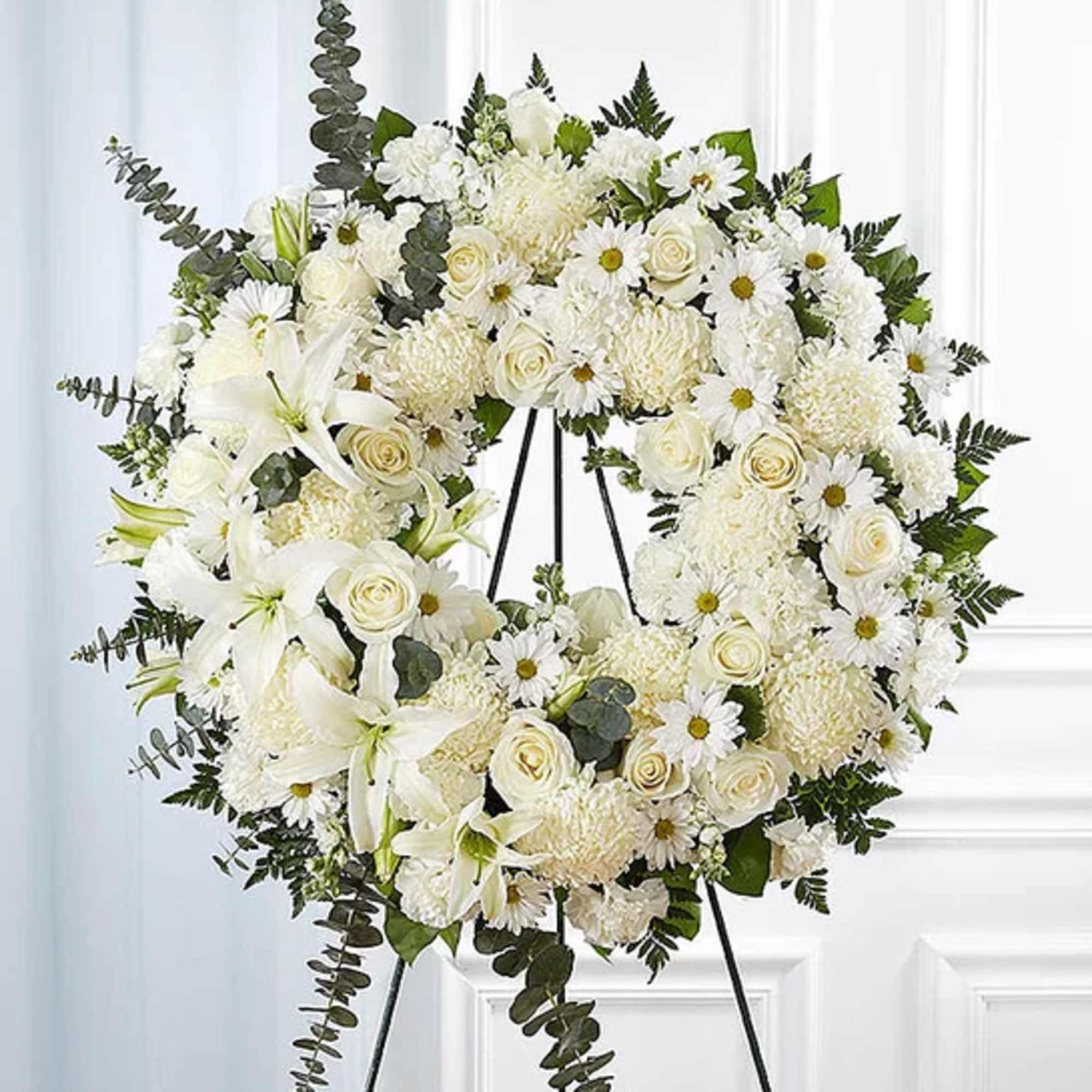 White funeral wreath with roses, lilies, and daisies on a black stand