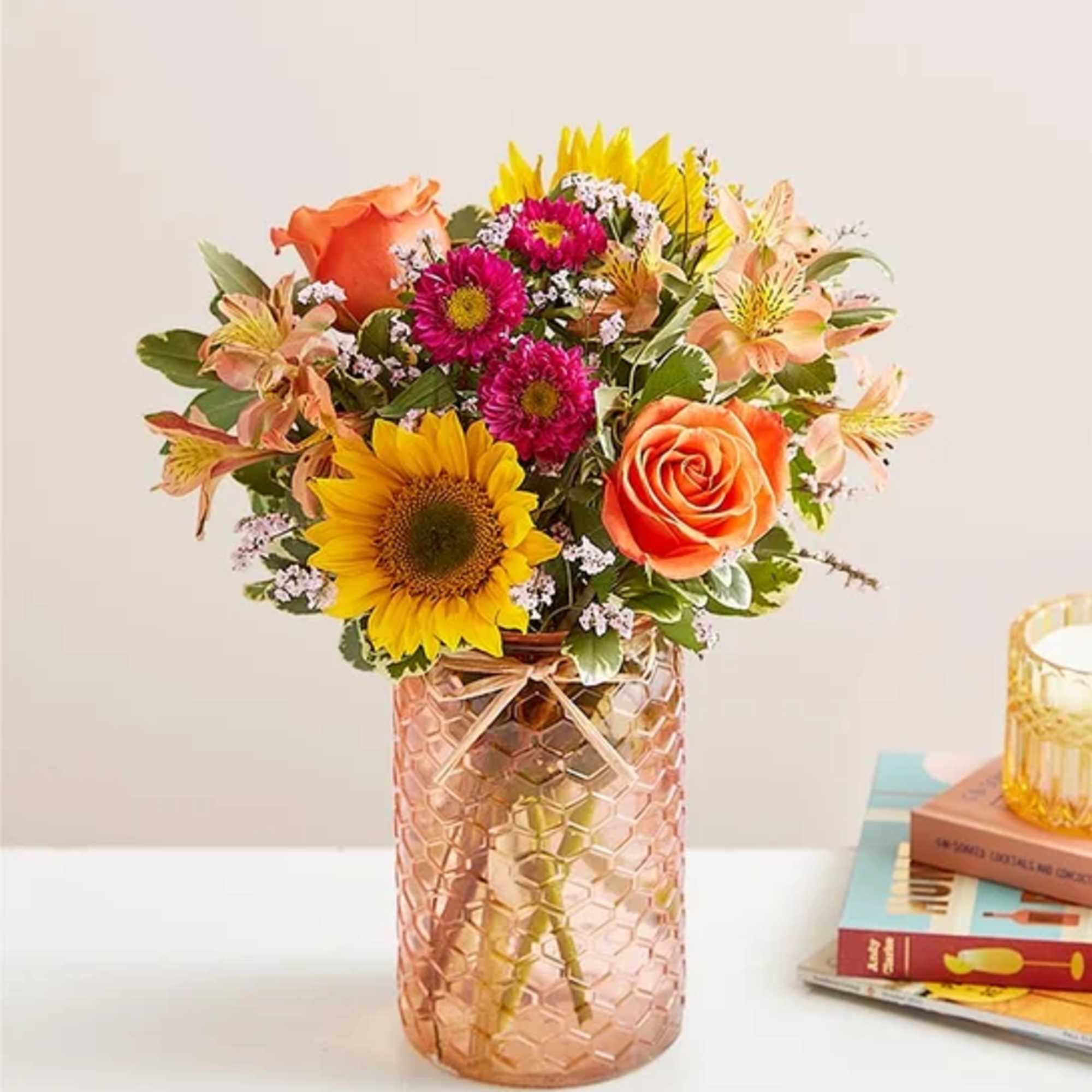 Bouquet of sunflowers, orange roses, and pink daisies in a textured glass vase