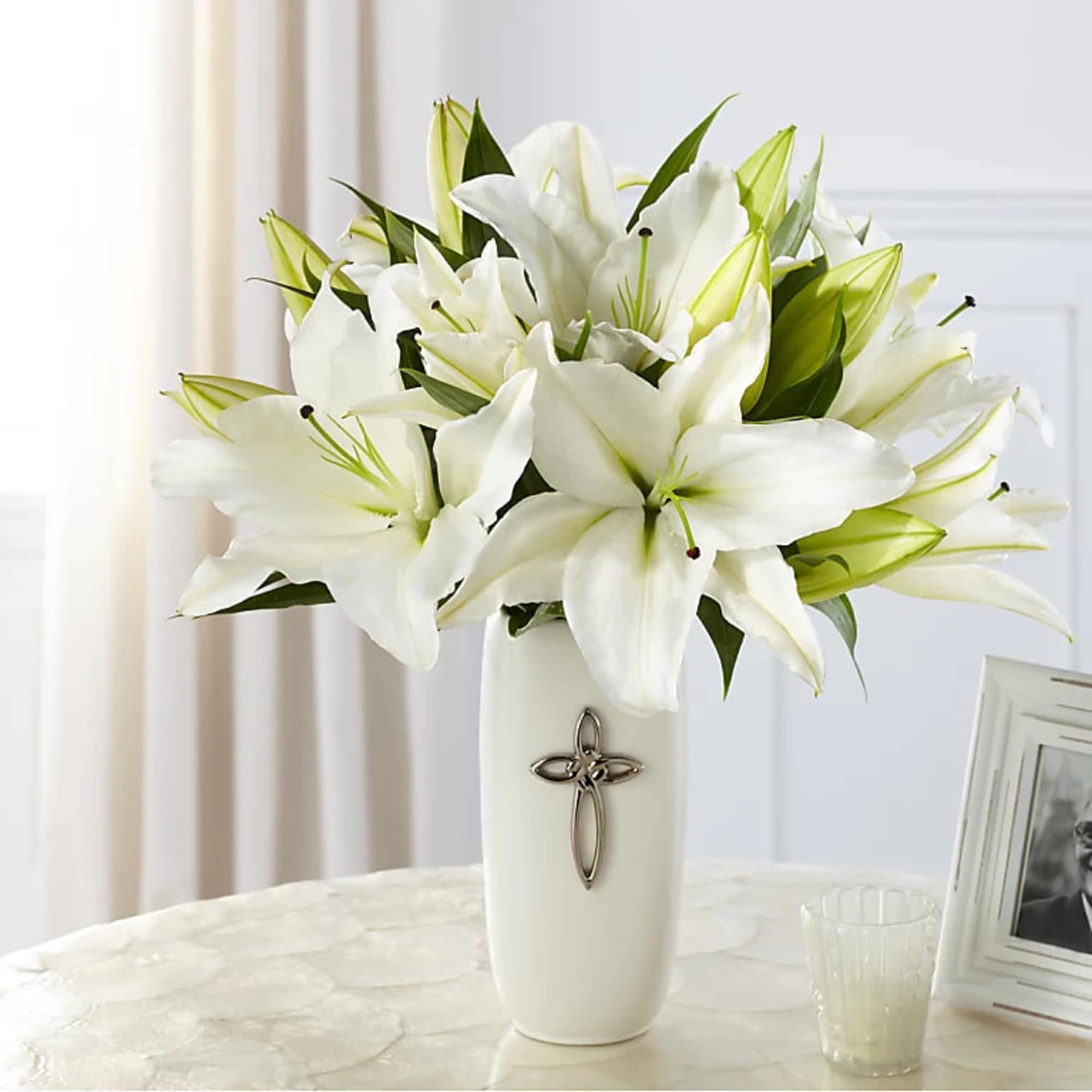 White lilies arranged in a tall white vase with a cross emblem