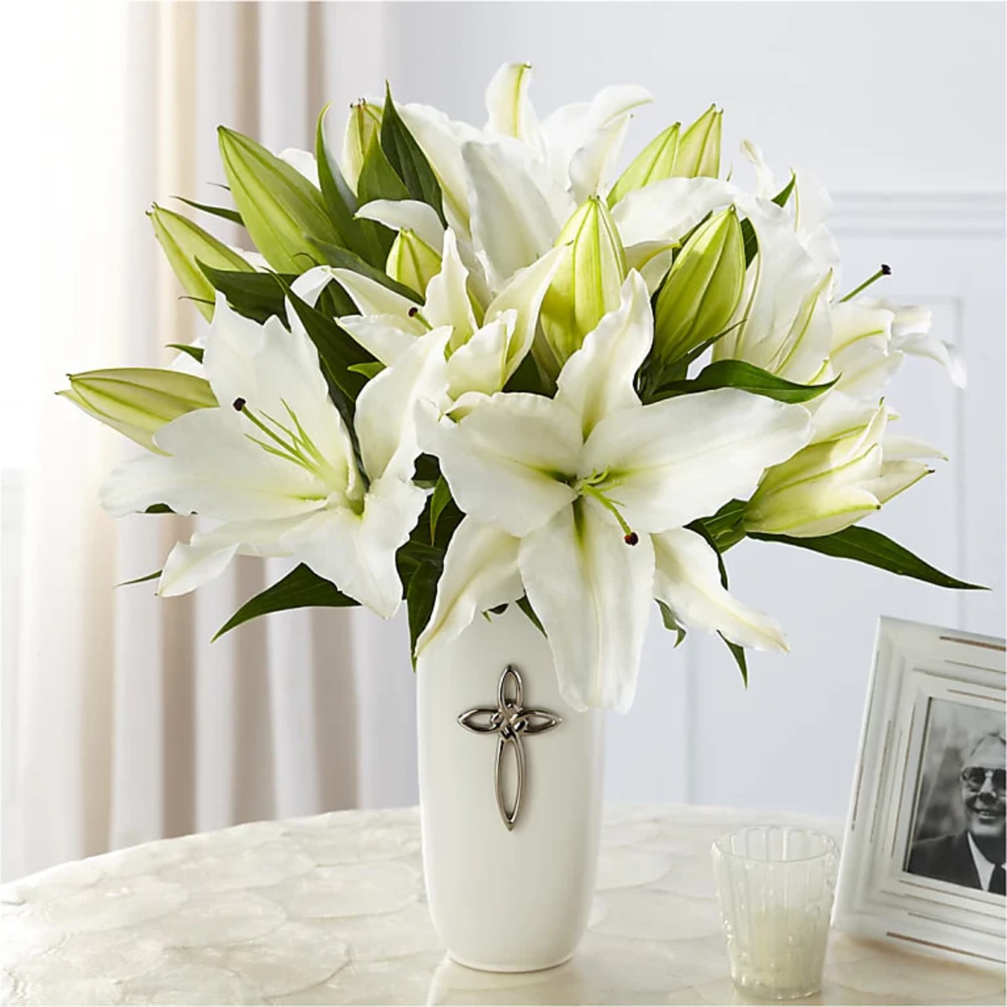 White lilies arranged in a white vase with a cross emblem