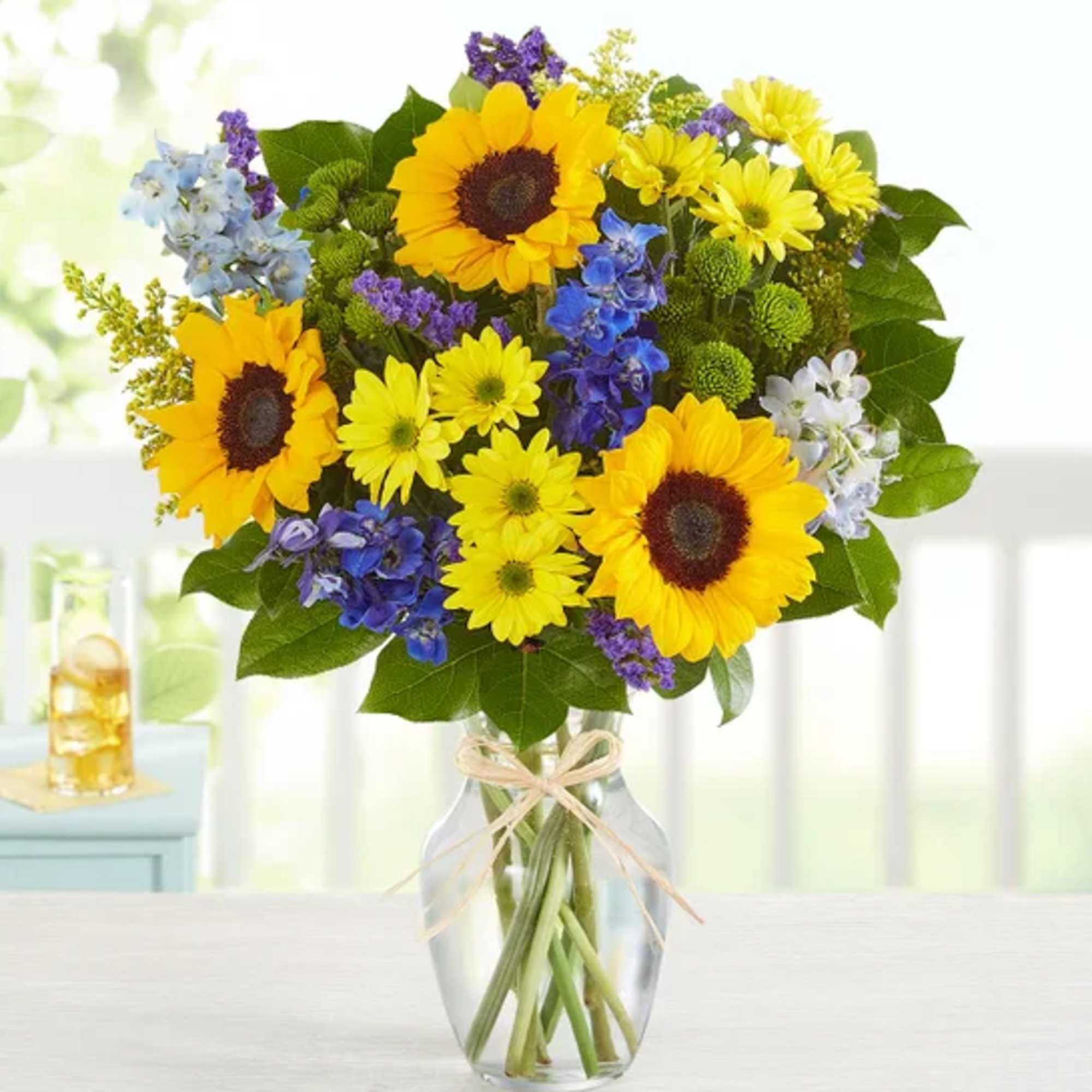 Bouquet of sunflowers, blue flowers, and yellow daisies in a glass vase