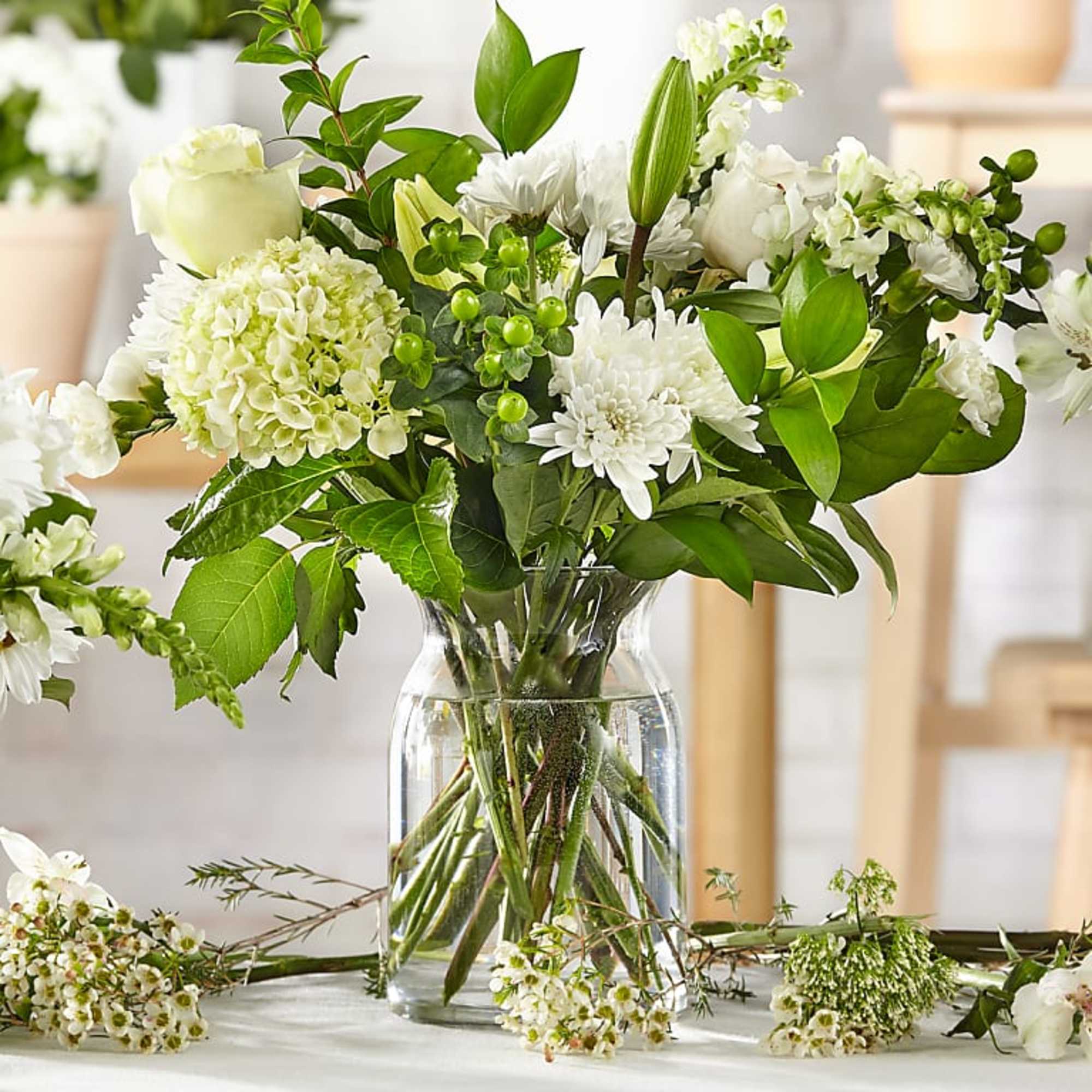 White floral arrangement in a clear glass vase with green foliage