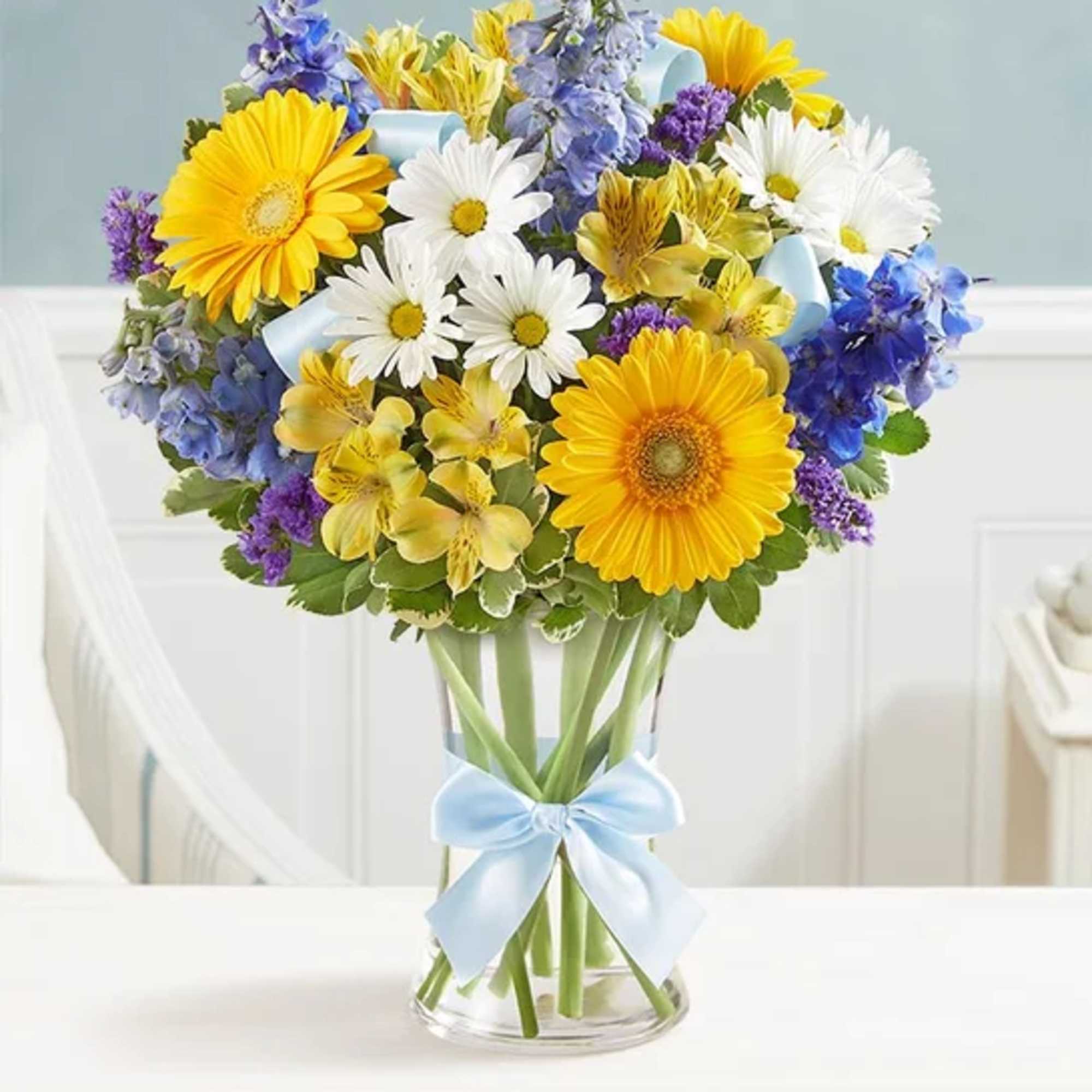 Bouquet of yellow and white daisies with blue and purple flowers in a glass vase