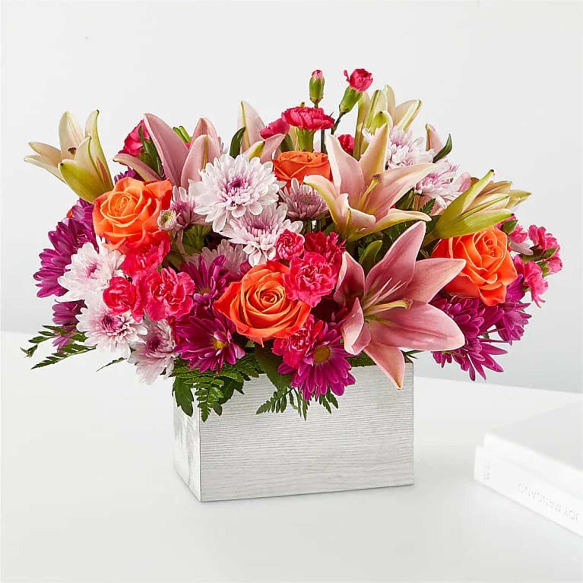 Mixed bouquet of orange roses, pink lilies, and chrysanthemums in a silver box