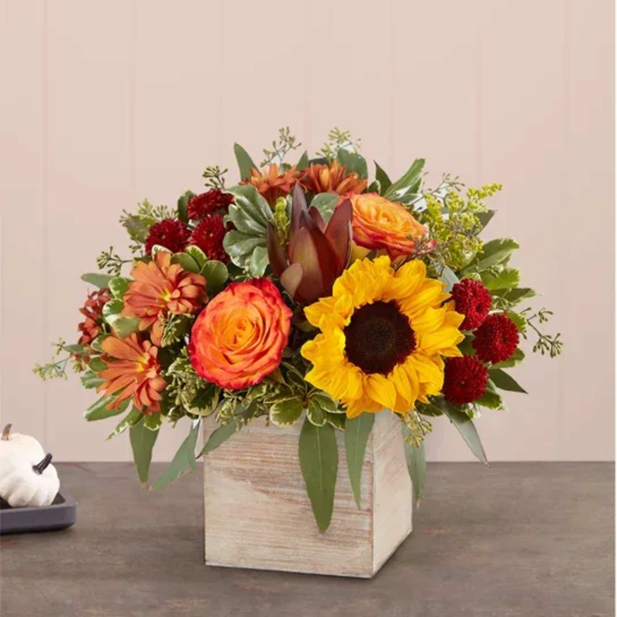 Autumn bouquet with sunflowers, roses, and red blooms in a wooden cube vase