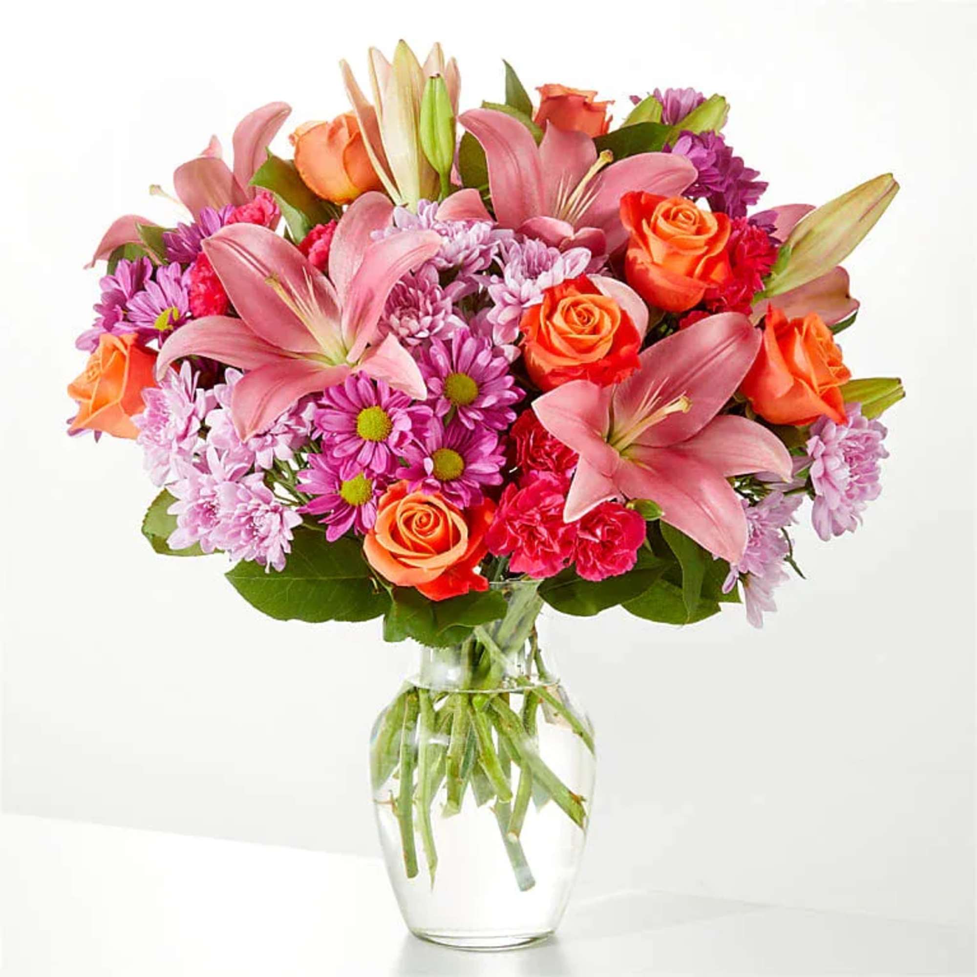 Mixed bouquet of pink lilies, roses, and purple daisies in a glass vase