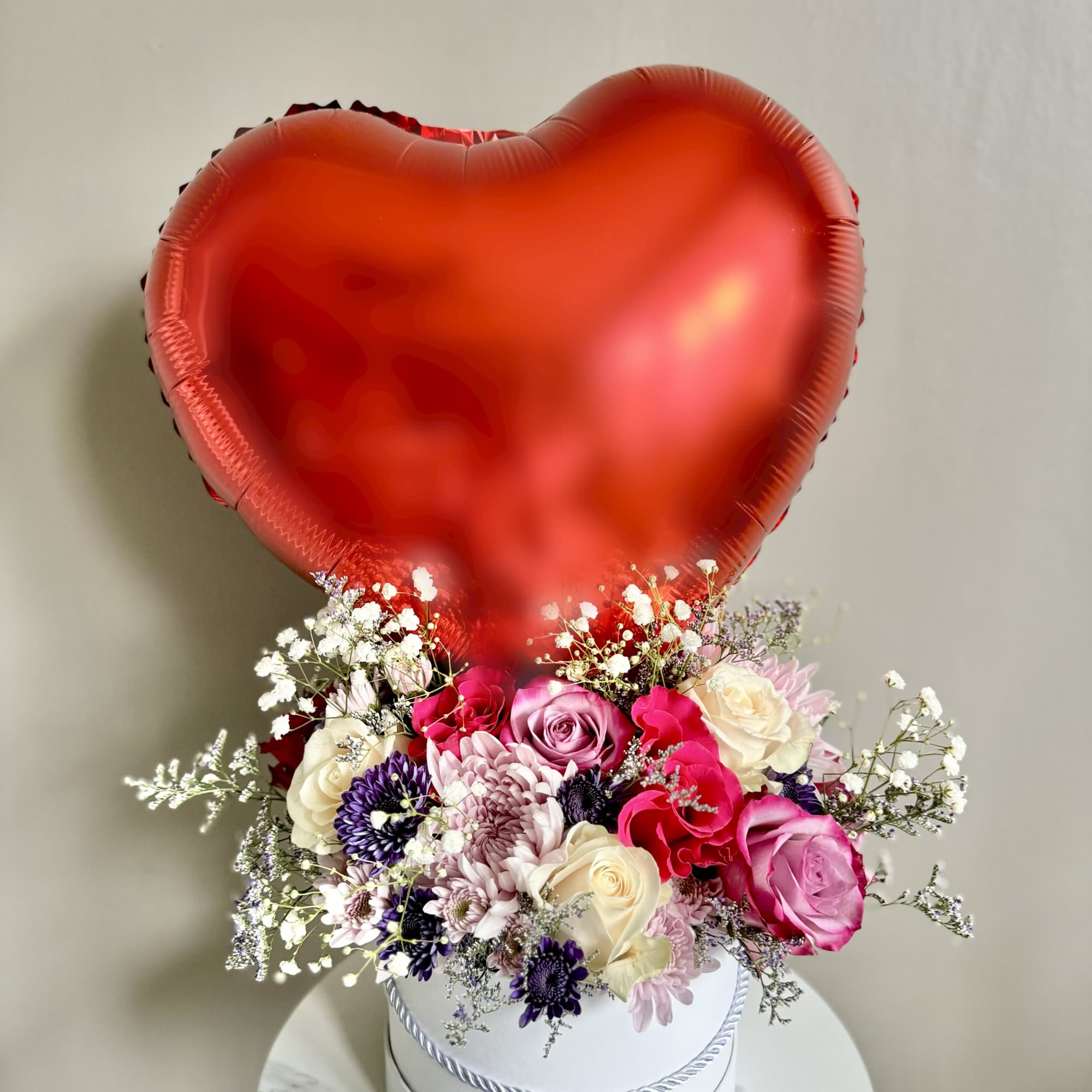 Heart-shaped red balloon above a mixed bouquet in a white hat box