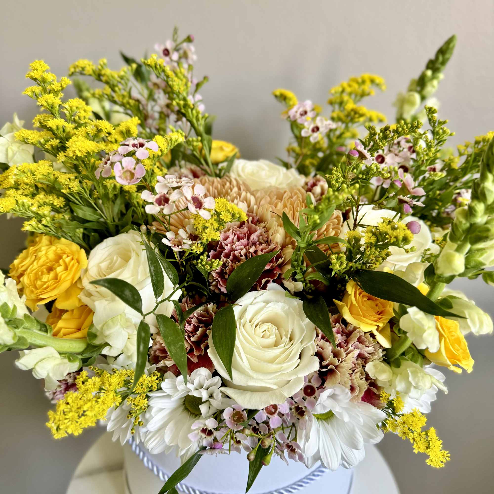 Mixed bouquet of yellow, white, and pink flowers in a white hatbox
