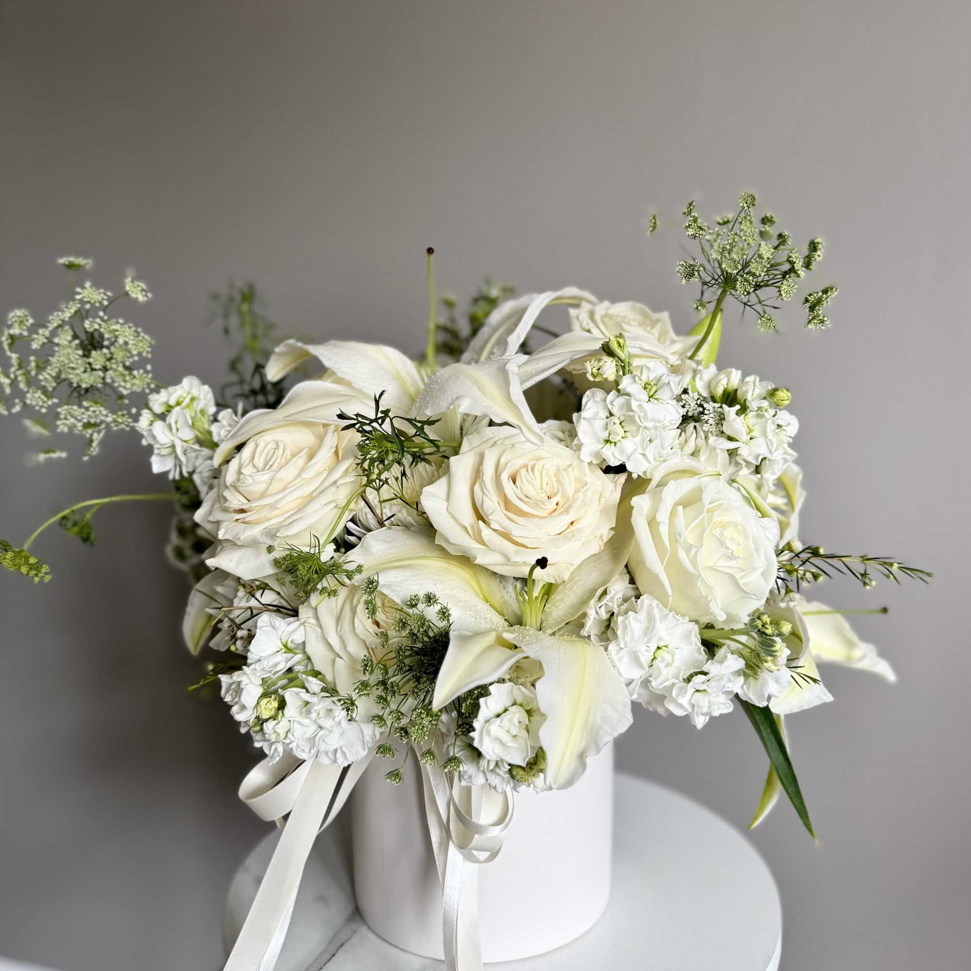 White roses and lilies arranged in a white box with ribbon