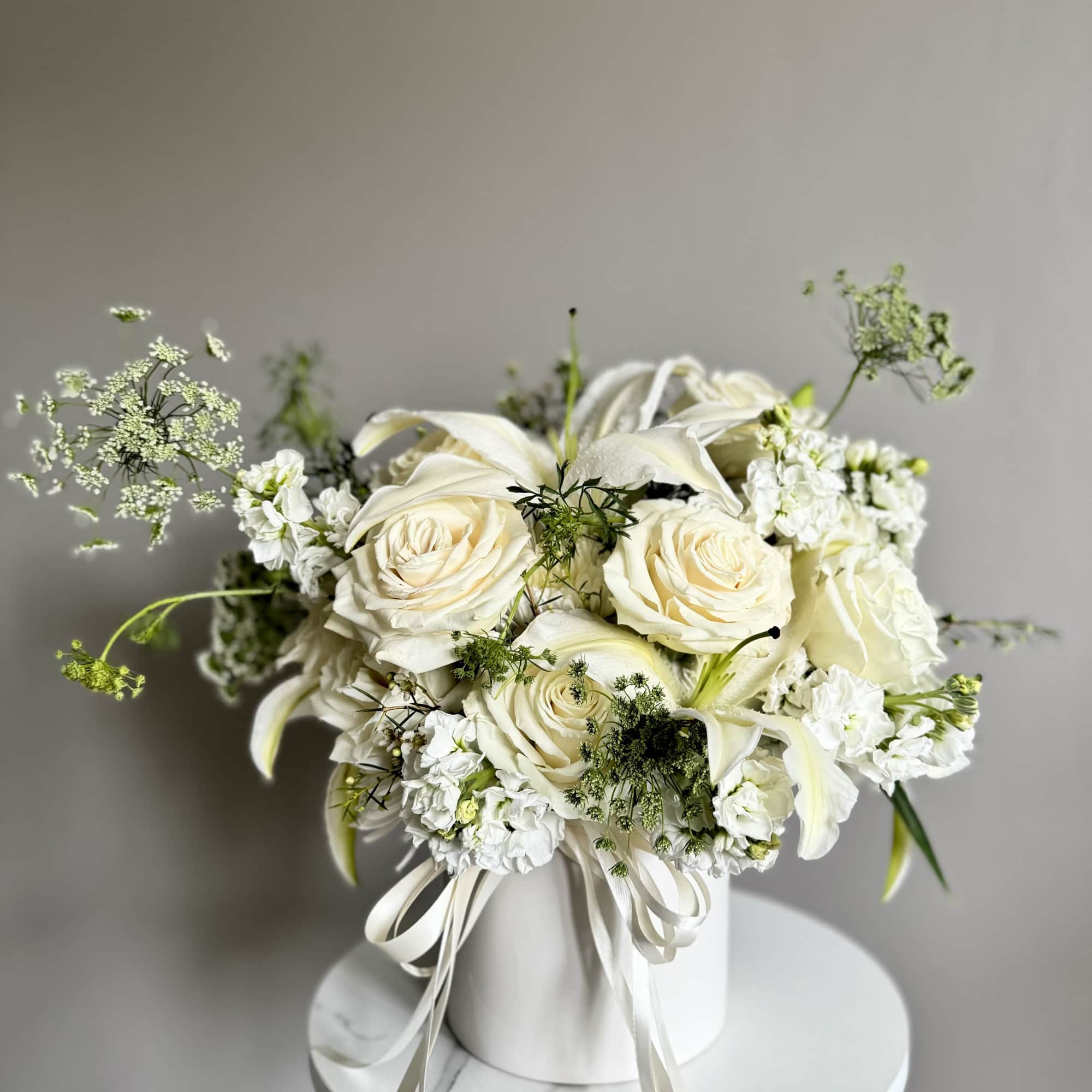 White roses and lilies arranged in a white hatbox with ribbon